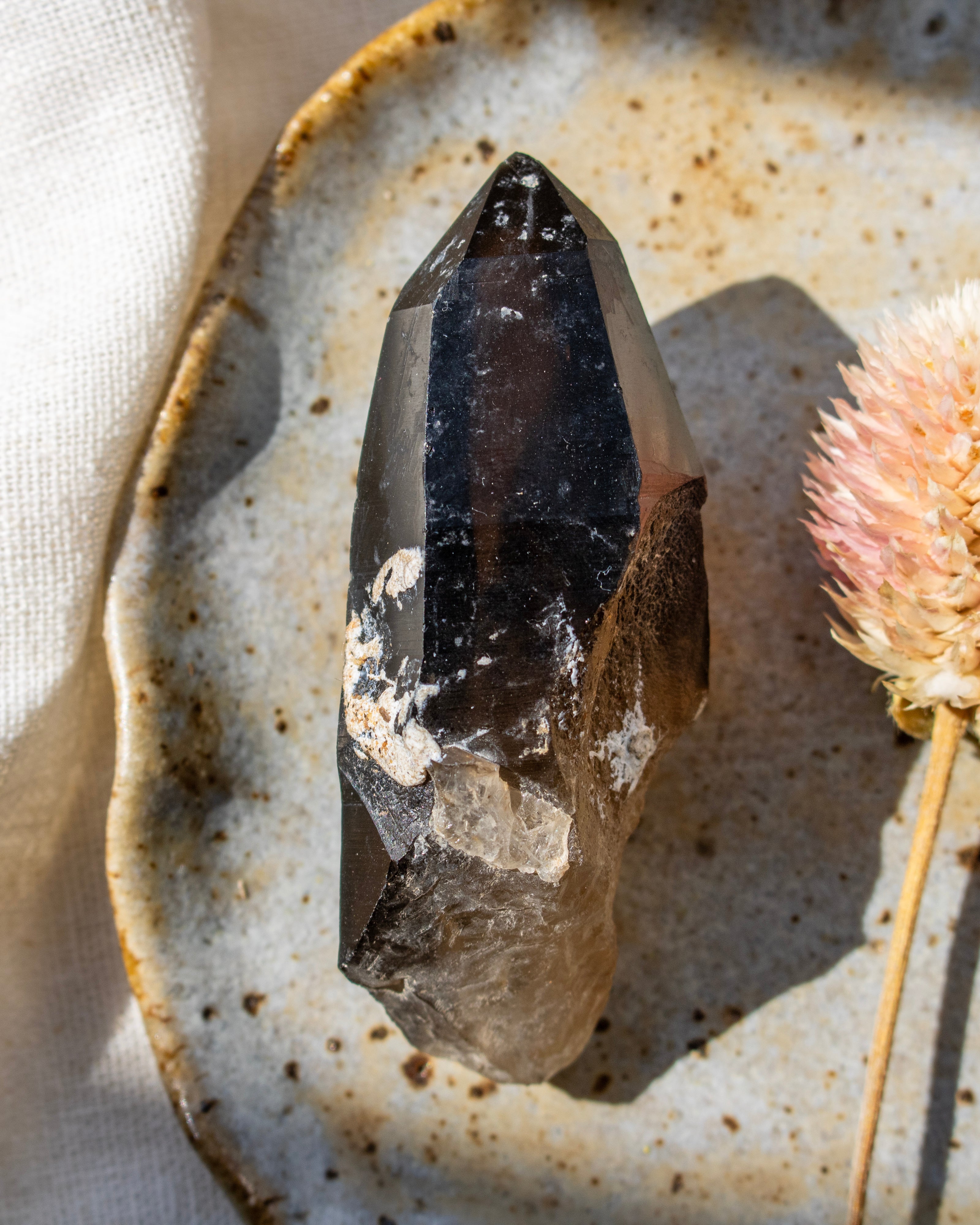 Mineral specimen on a textured ceramic plate with a dried flower