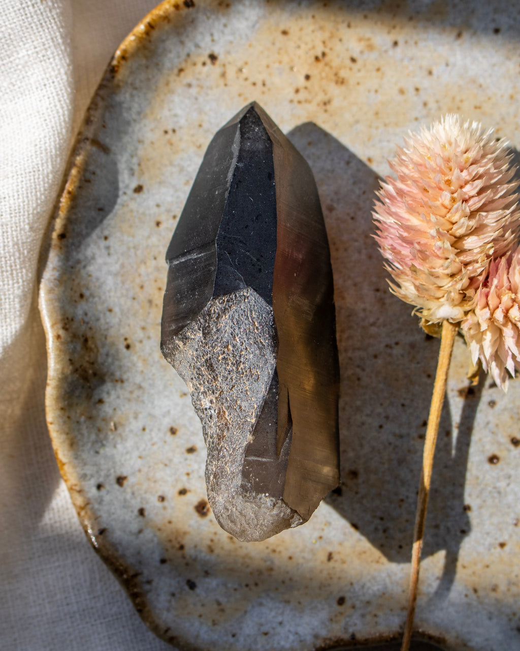 Mineral specimen on a textured ceramic plate with a dried flower