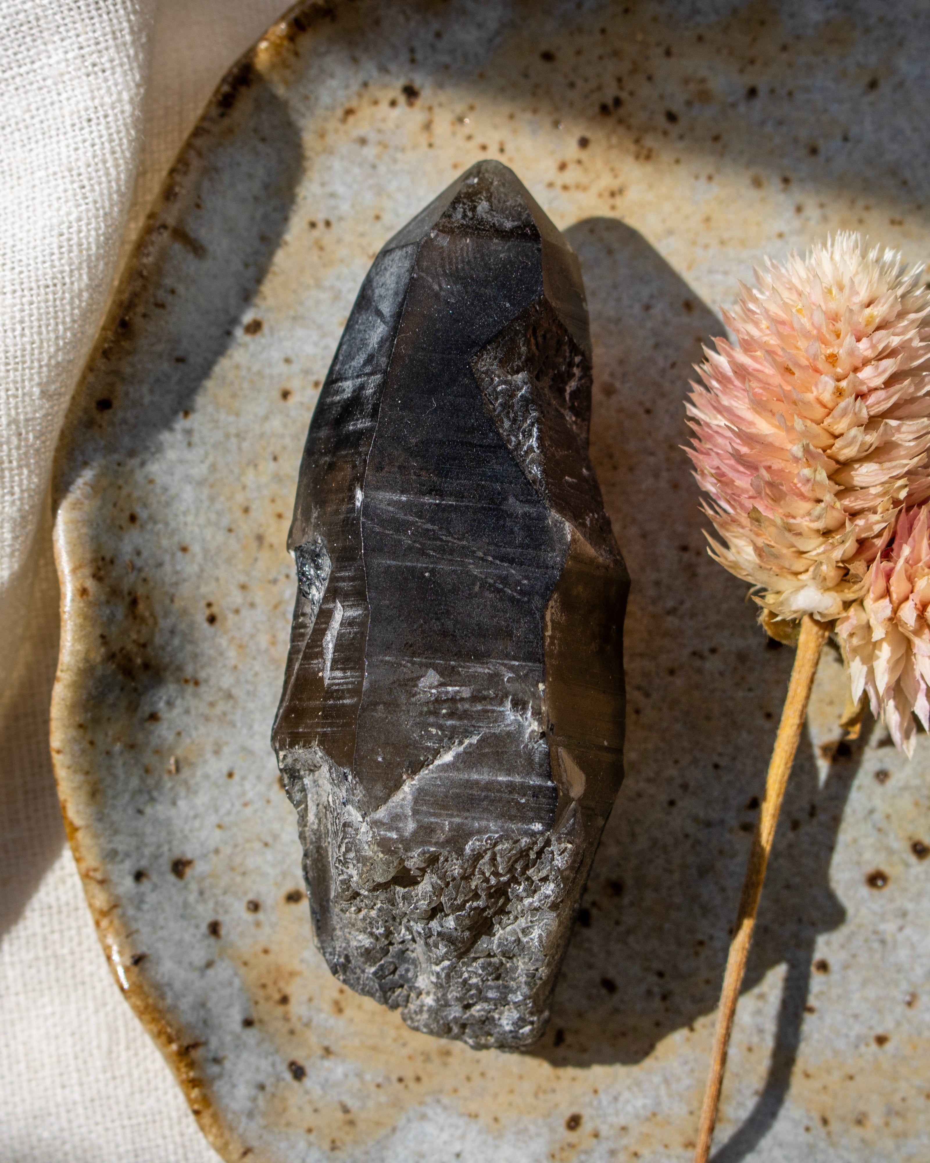 Raw crystal on a textured ceramic plate with a dried flower