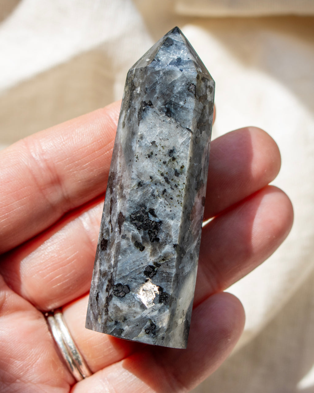 Hand holding a crystal with a textured surface and black inclusions.