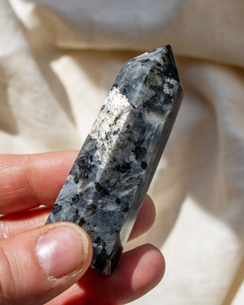 Hand holding a crystal with a white and gray pattern against a beige fabric background