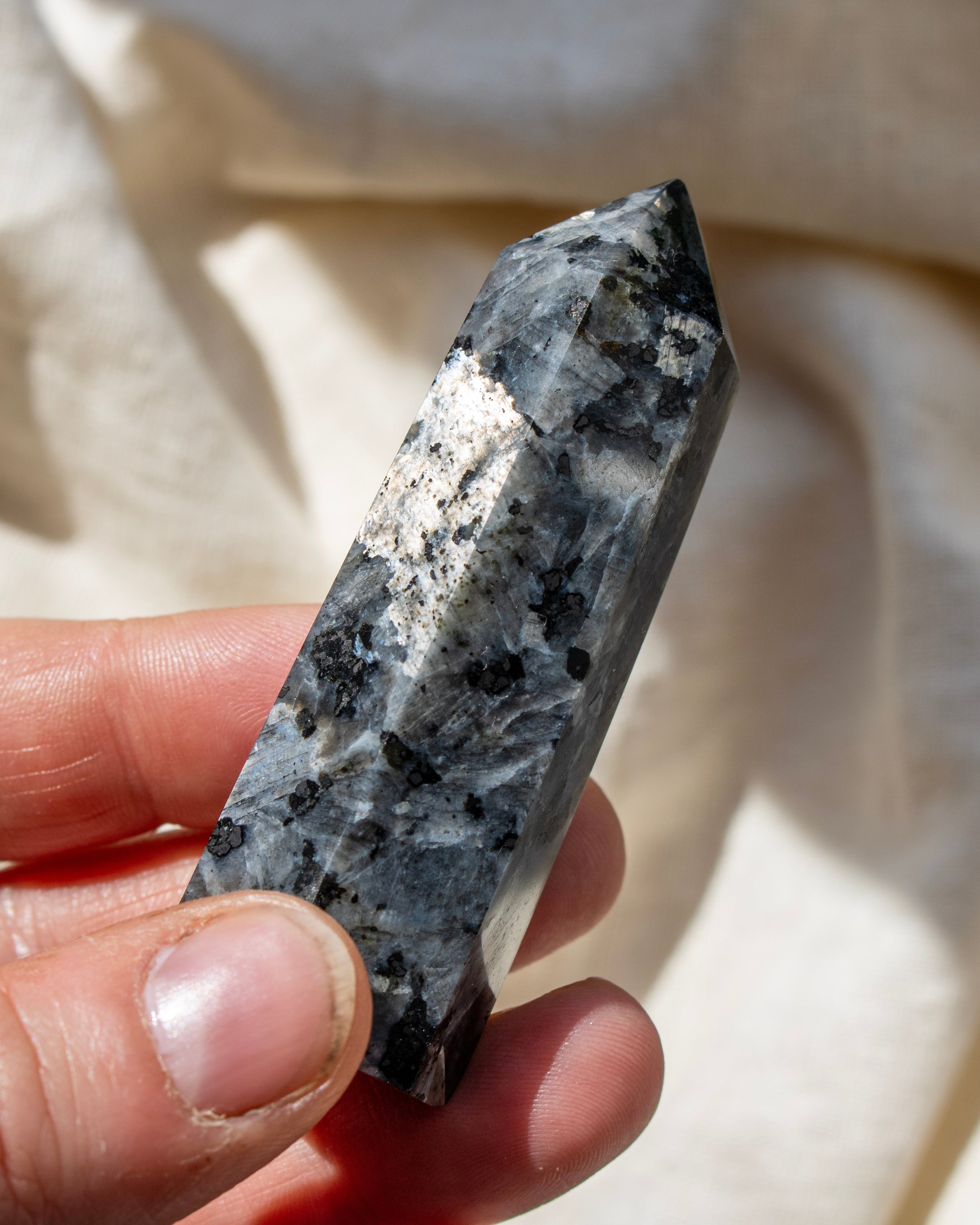 Hand holding a crystal with a white and gray pattern against a beige fabric background