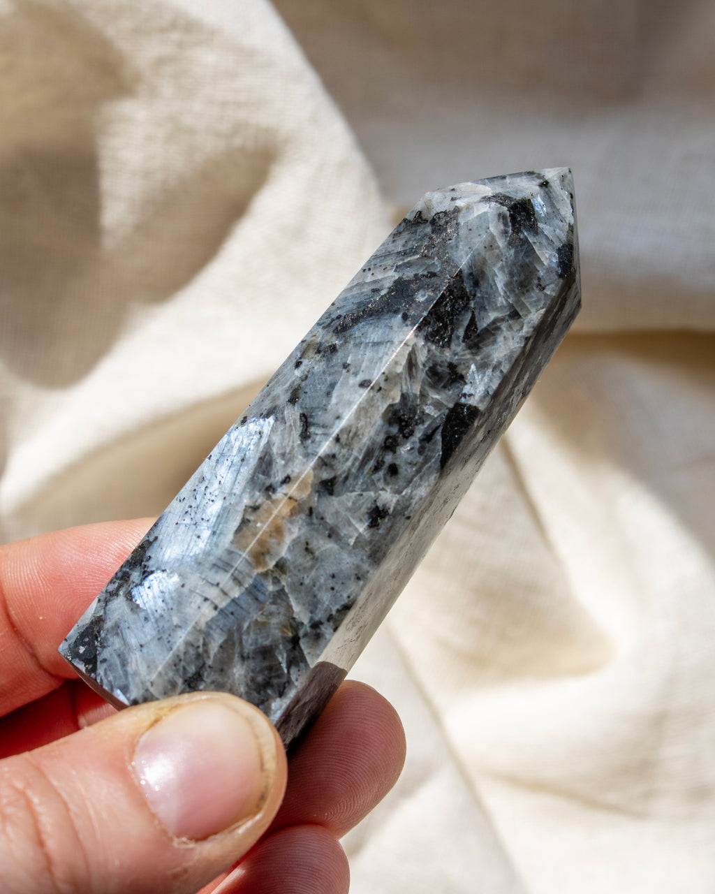 Hand holding a crystal with a textured surface against a neutral background