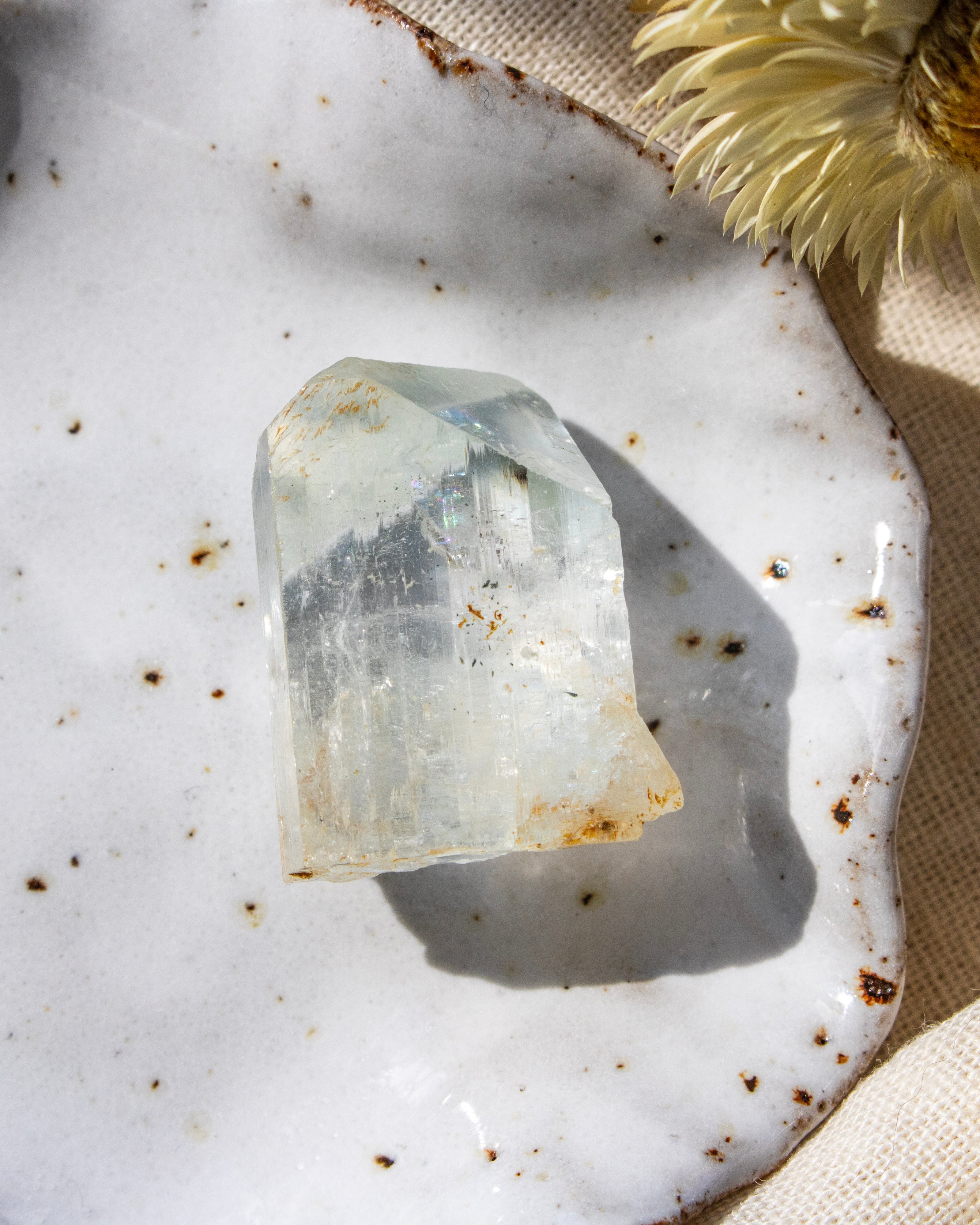 Clear crystal on a textured white surface with a yellow flower in the corner
