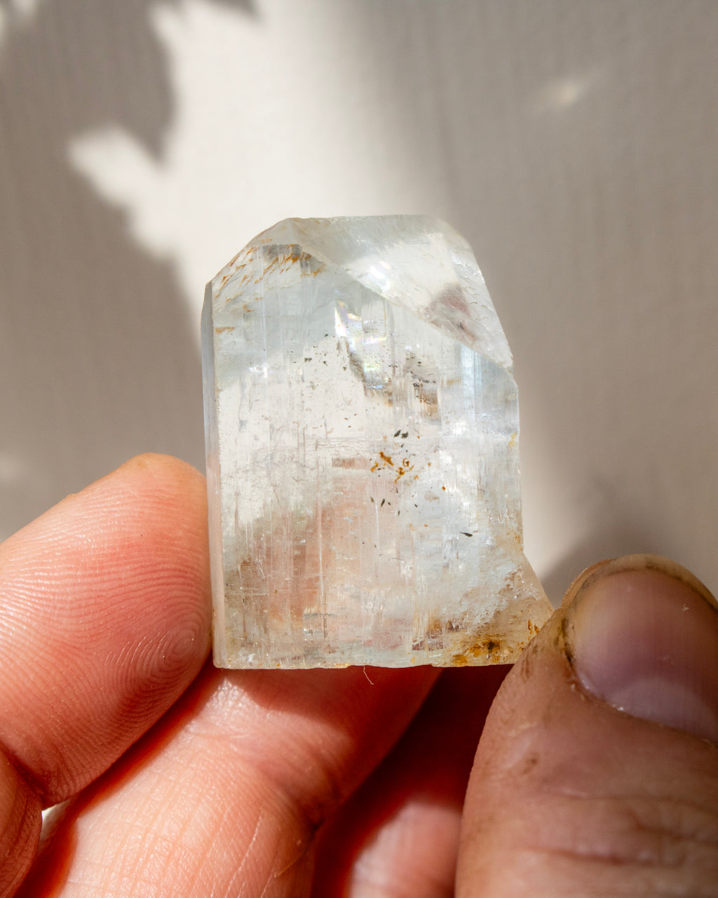 Clear crystal held between fingers against a neutral background