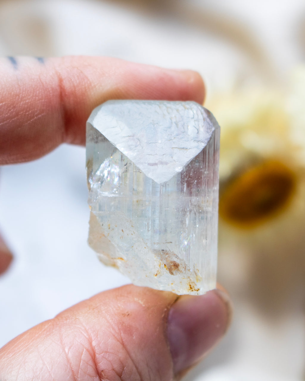 Clear crystal held between fingers against a neutral background