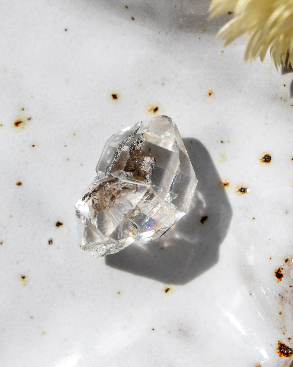 Clear crystal on a textured white surface with specks of brown