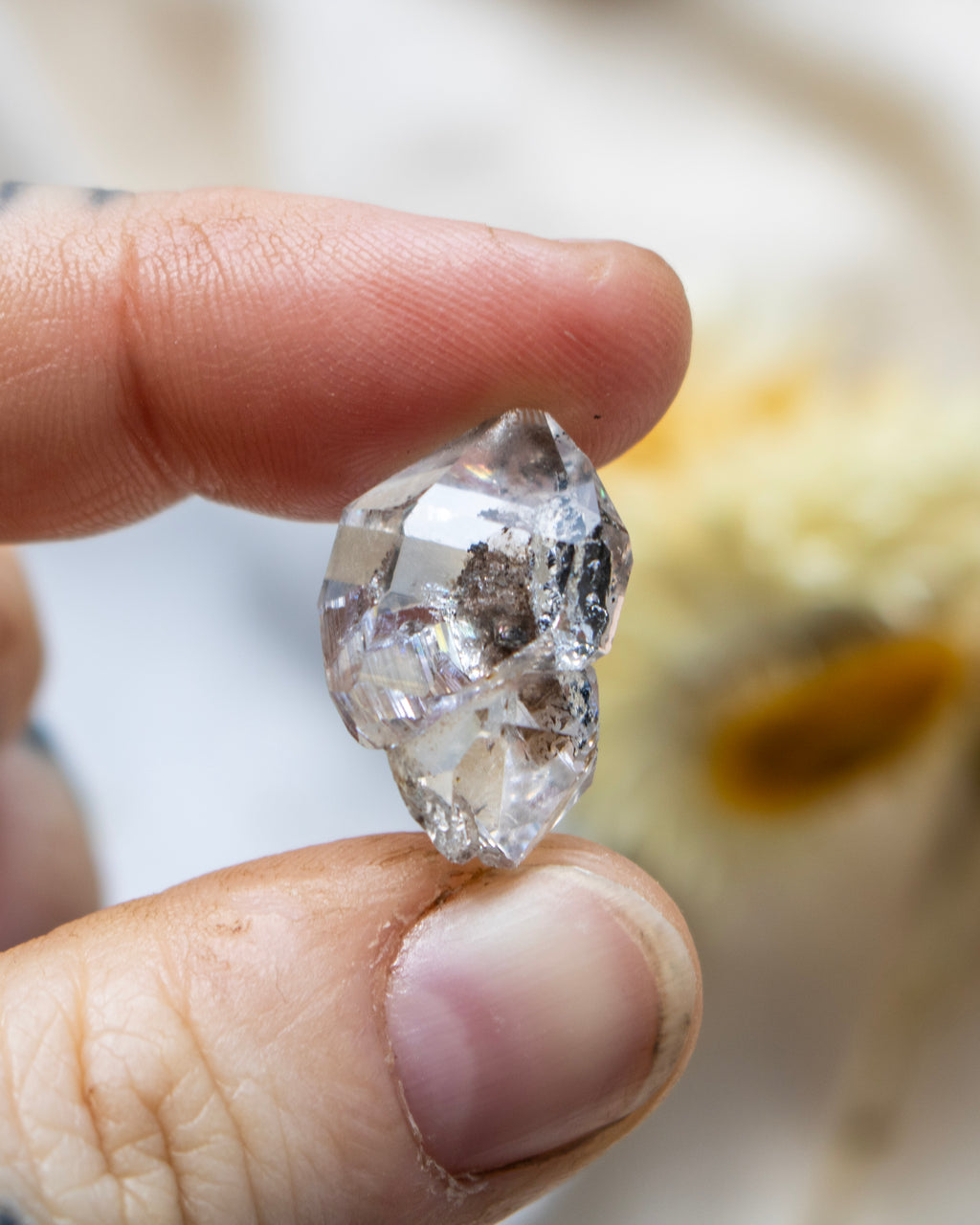 Raw diamond quartz held between fingers with a blurred background