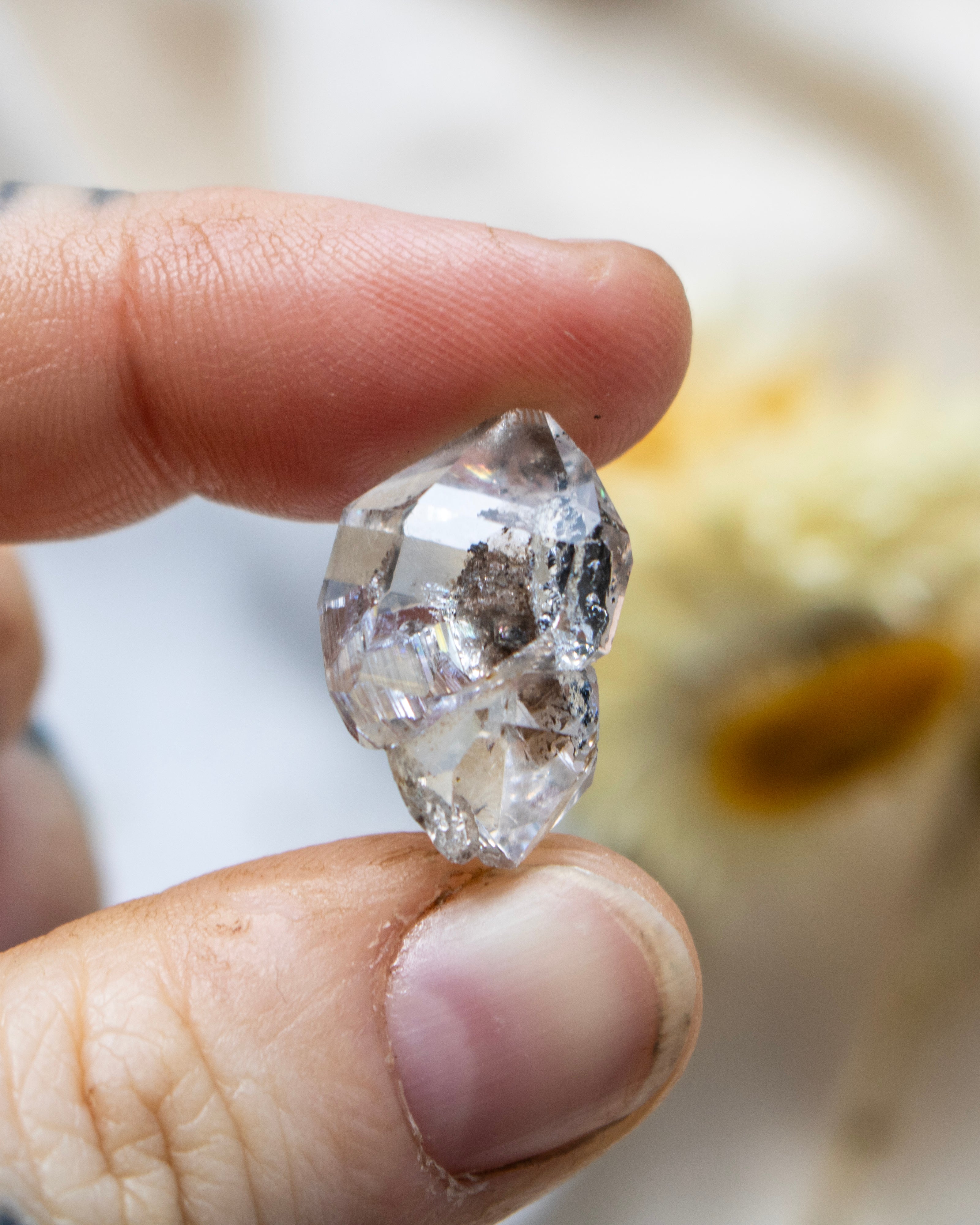 Raw diamond quartz held between fingers with a blurred background