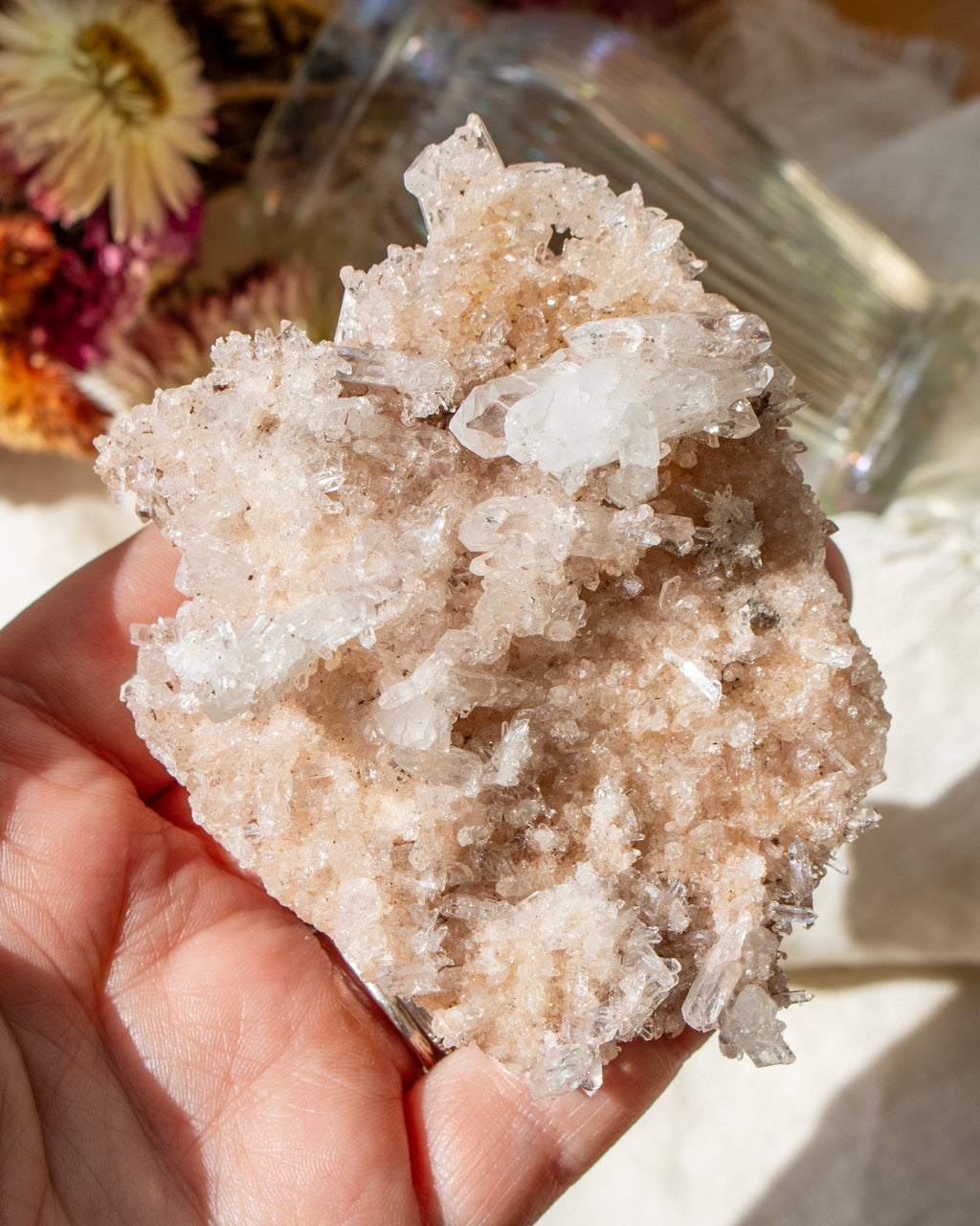 Hand holding a large crystal cluster against a neutral background