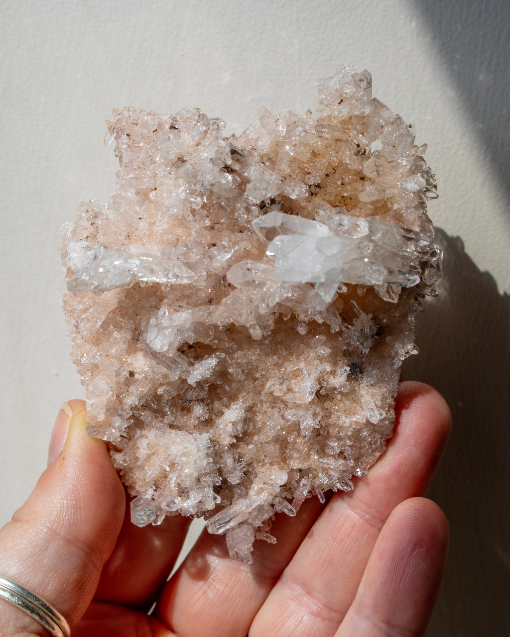 Hand holding a large crystal cluster against a neutral background