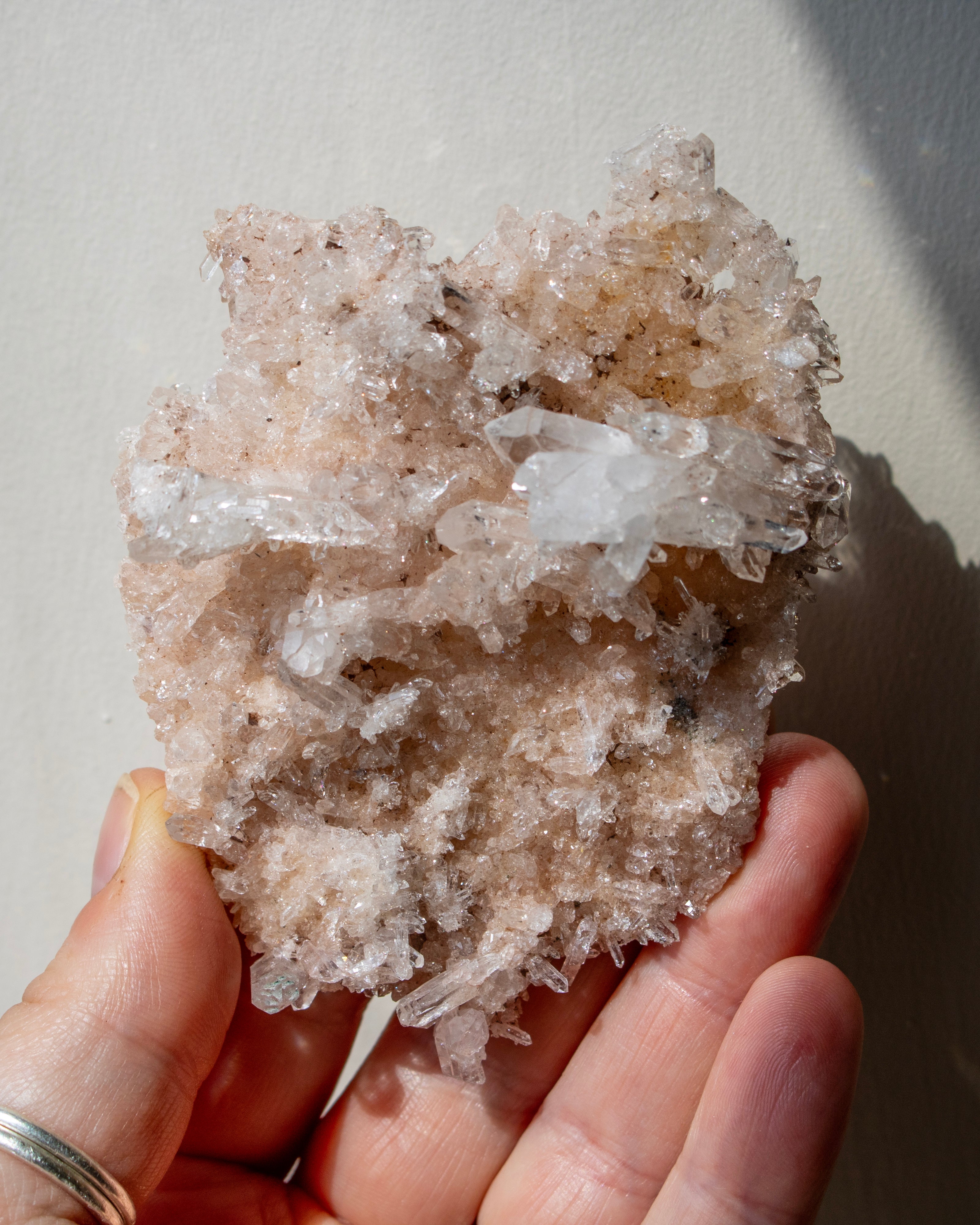 Hand holding a large crystal cluster against a neutral background