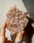 Hand holding a large crystal cluster against a neutral background