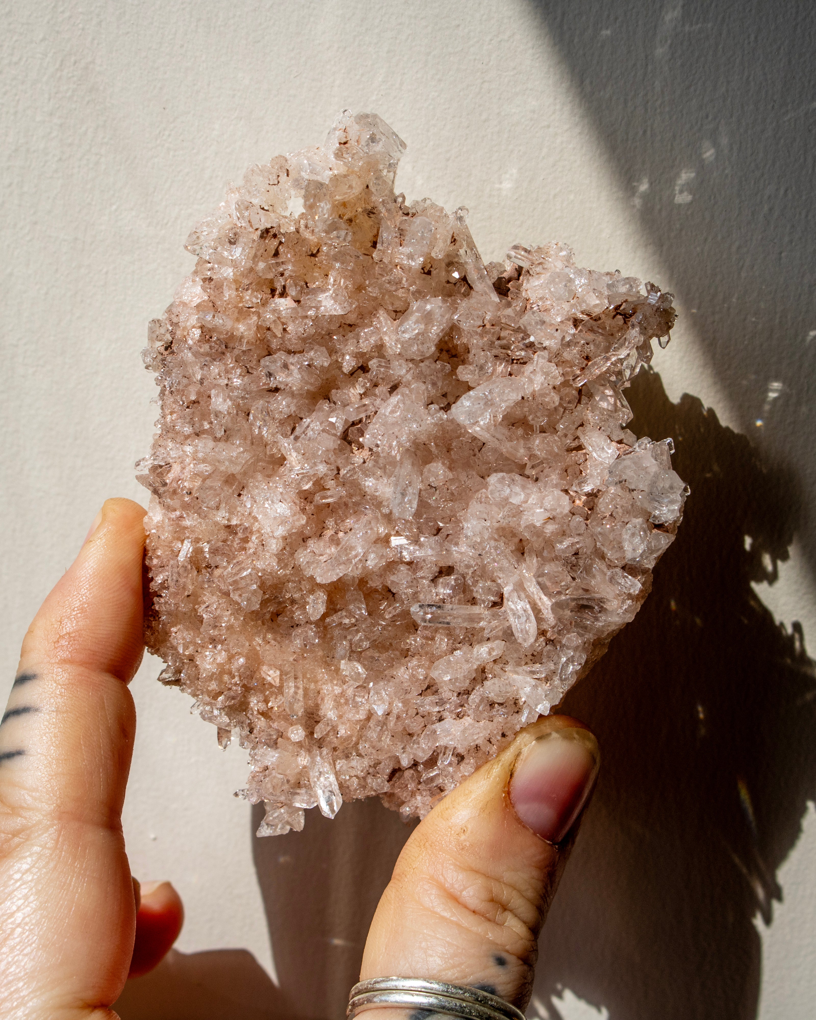 Hand holding a large crystal cluster against a neutral background