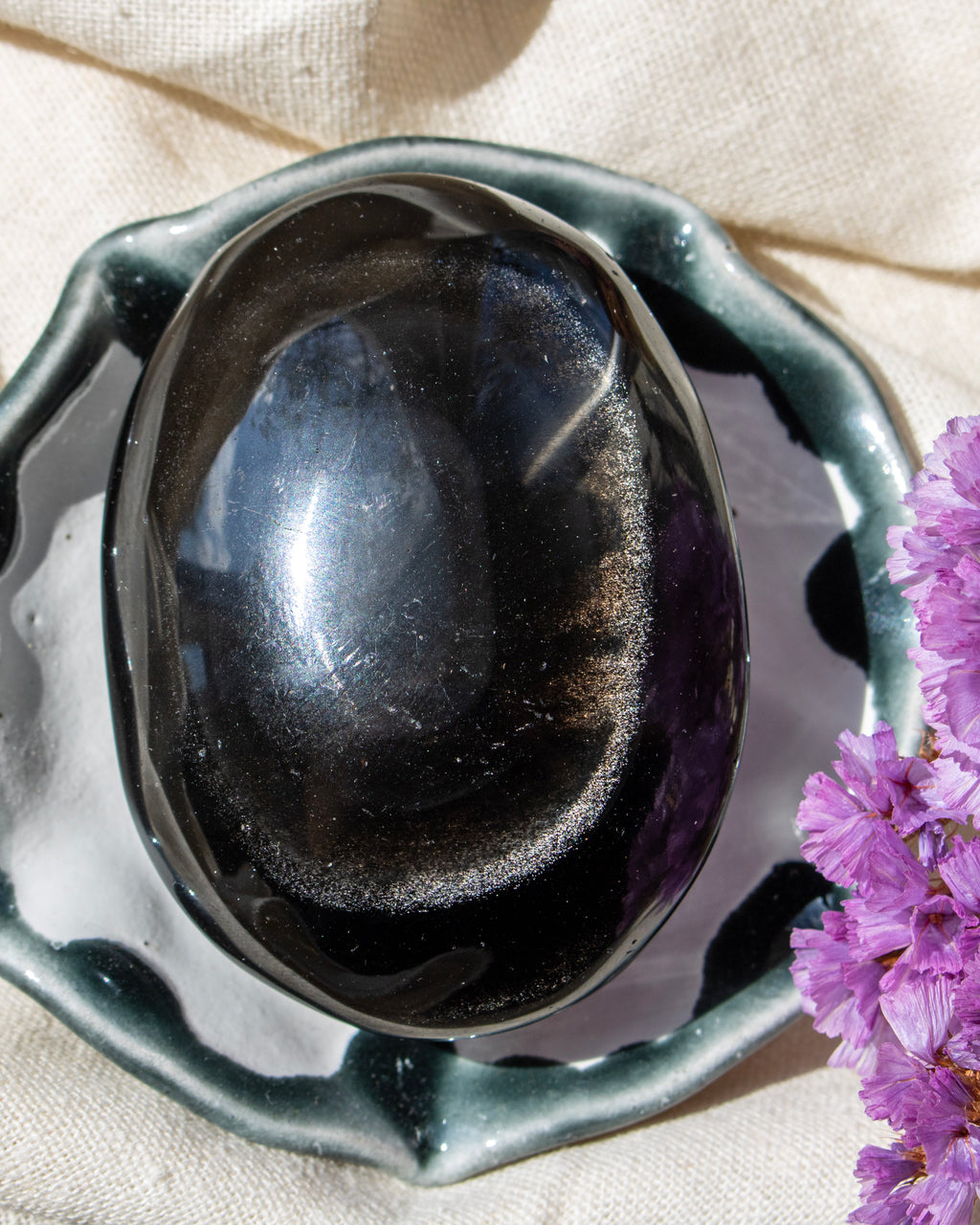 Black stone in a decorative bowl with purple flowers on a beige fabric background