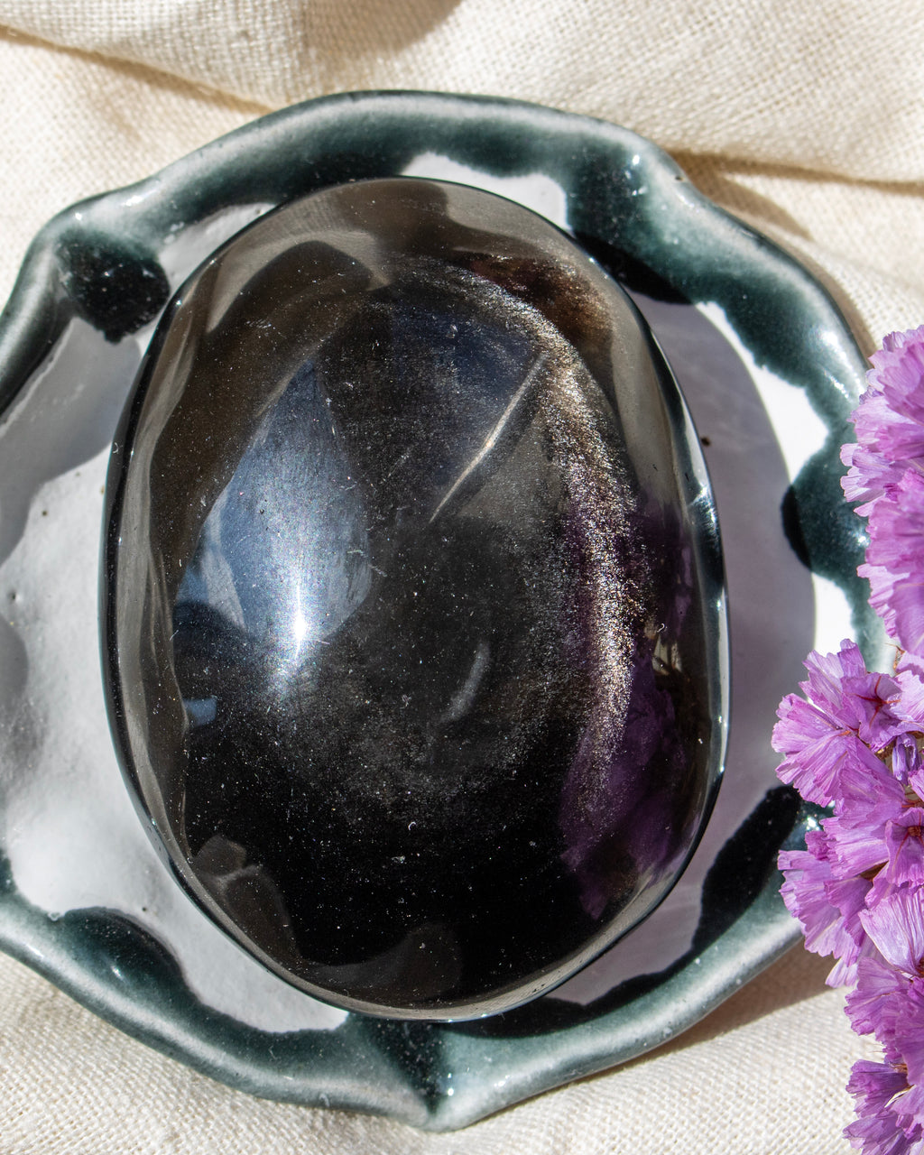 Black stone in a decorative bowl with purple flowers on a beige fabric background