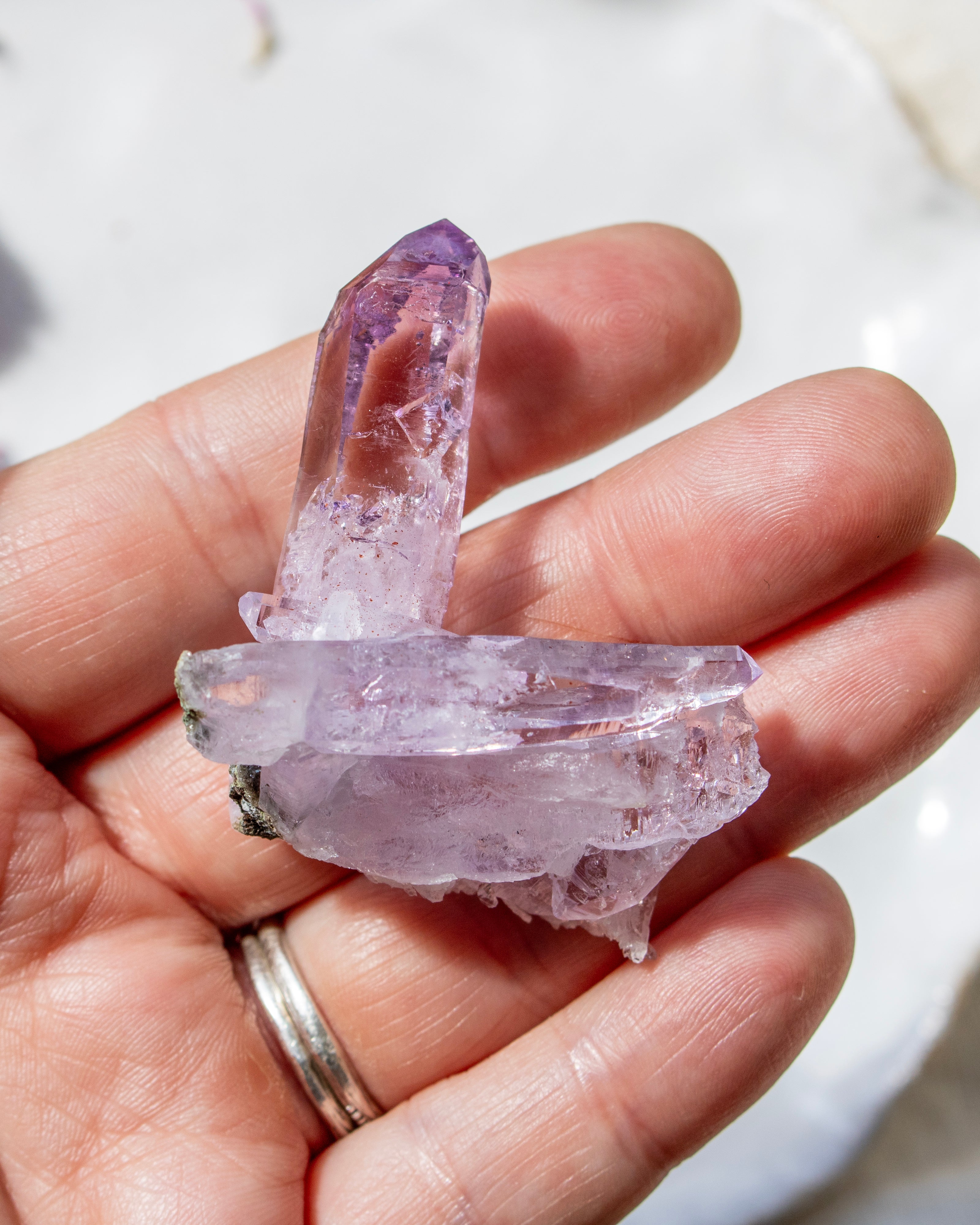 Hand holding a clear crystal with purple tint against a blurred background