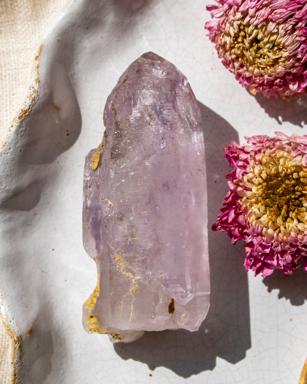 Amethyst crystal on a white surface with pink flowers