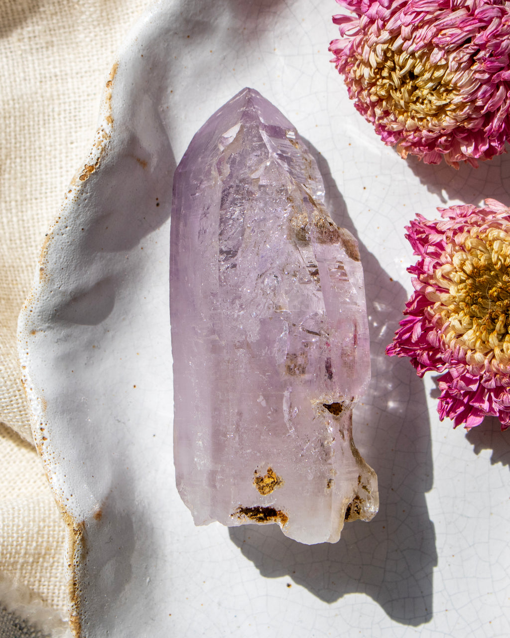 Amethyst crystal on a white surface with pink flowers