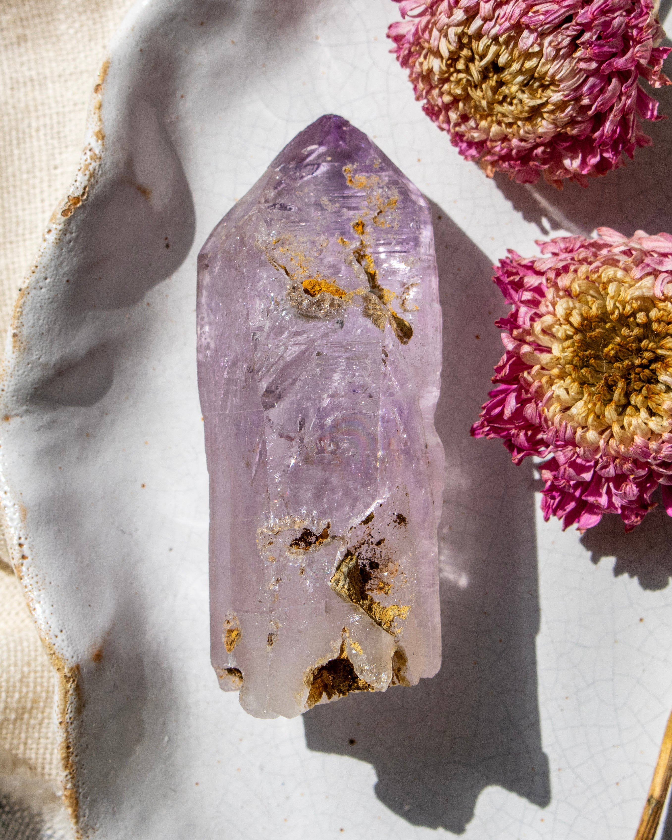 Amethyst crystal with gold inclusions on a white surface with pink flowers.