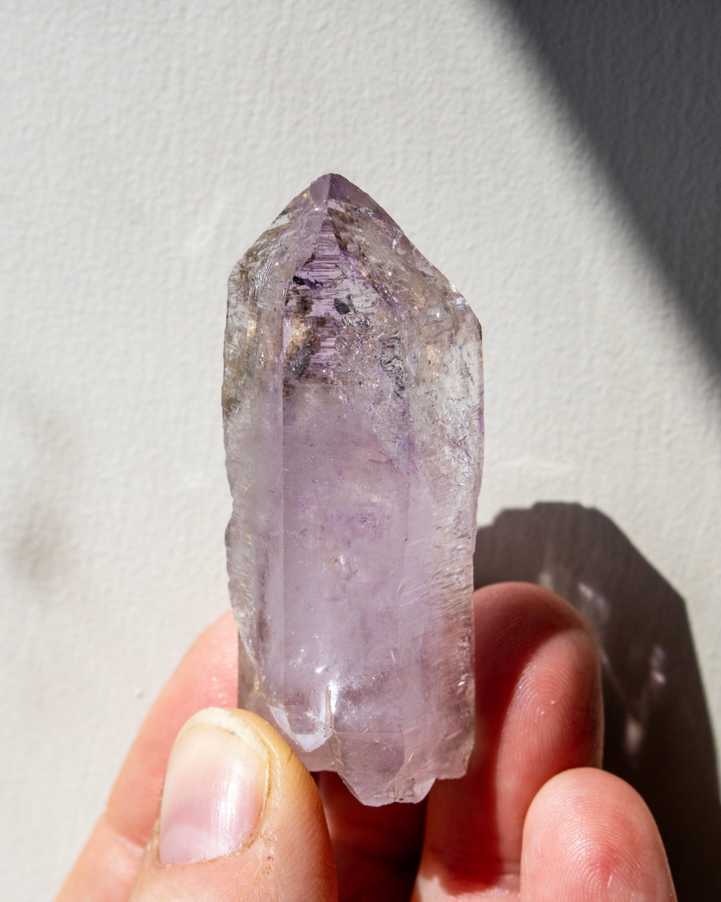 Amethyst crystal held in a hand against a neutral background
