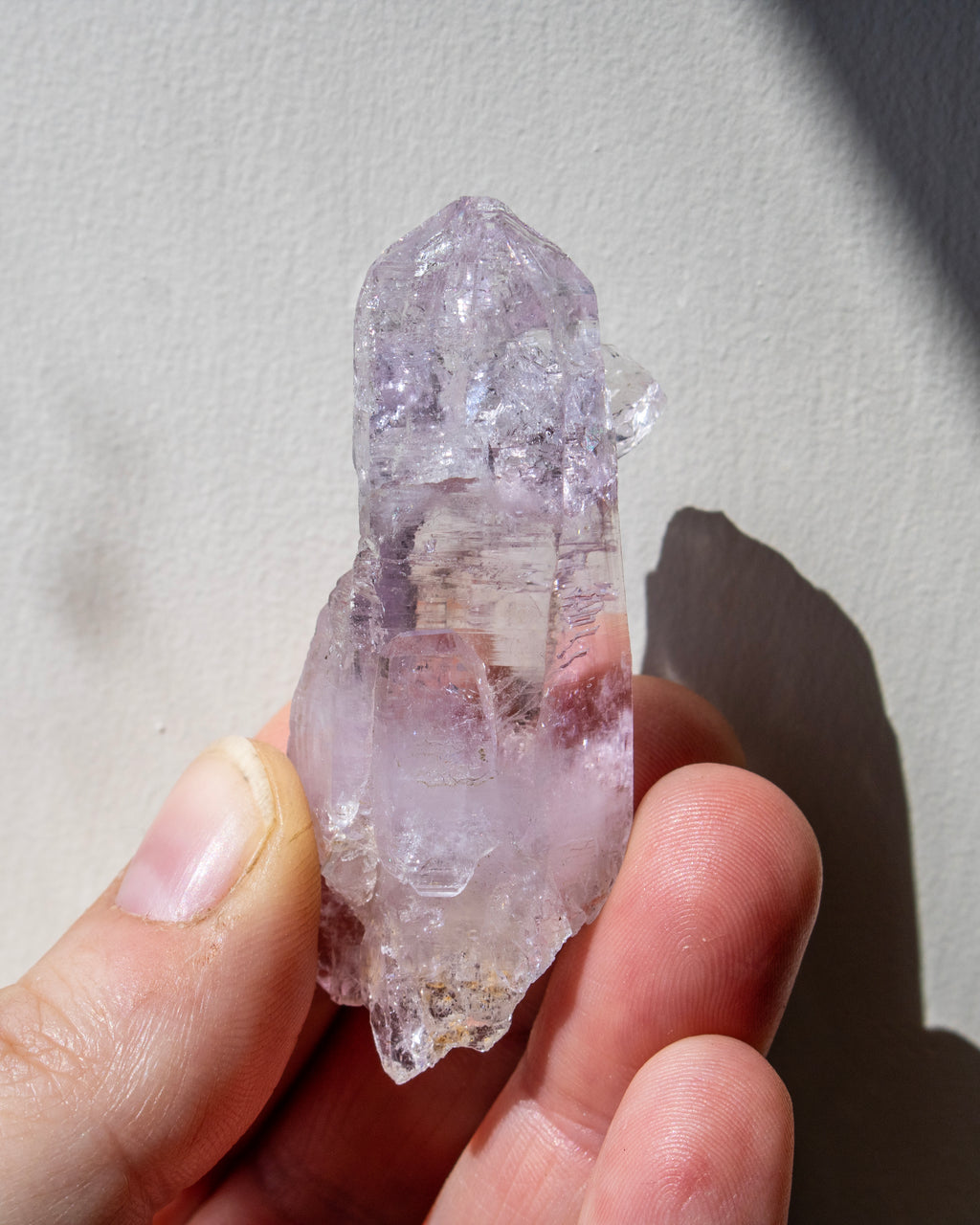 Hand holding a clear crystal with purple and white markings against a neutral background