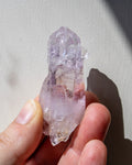 Hand holding a clear crystal with purple and white markings against a neutral background