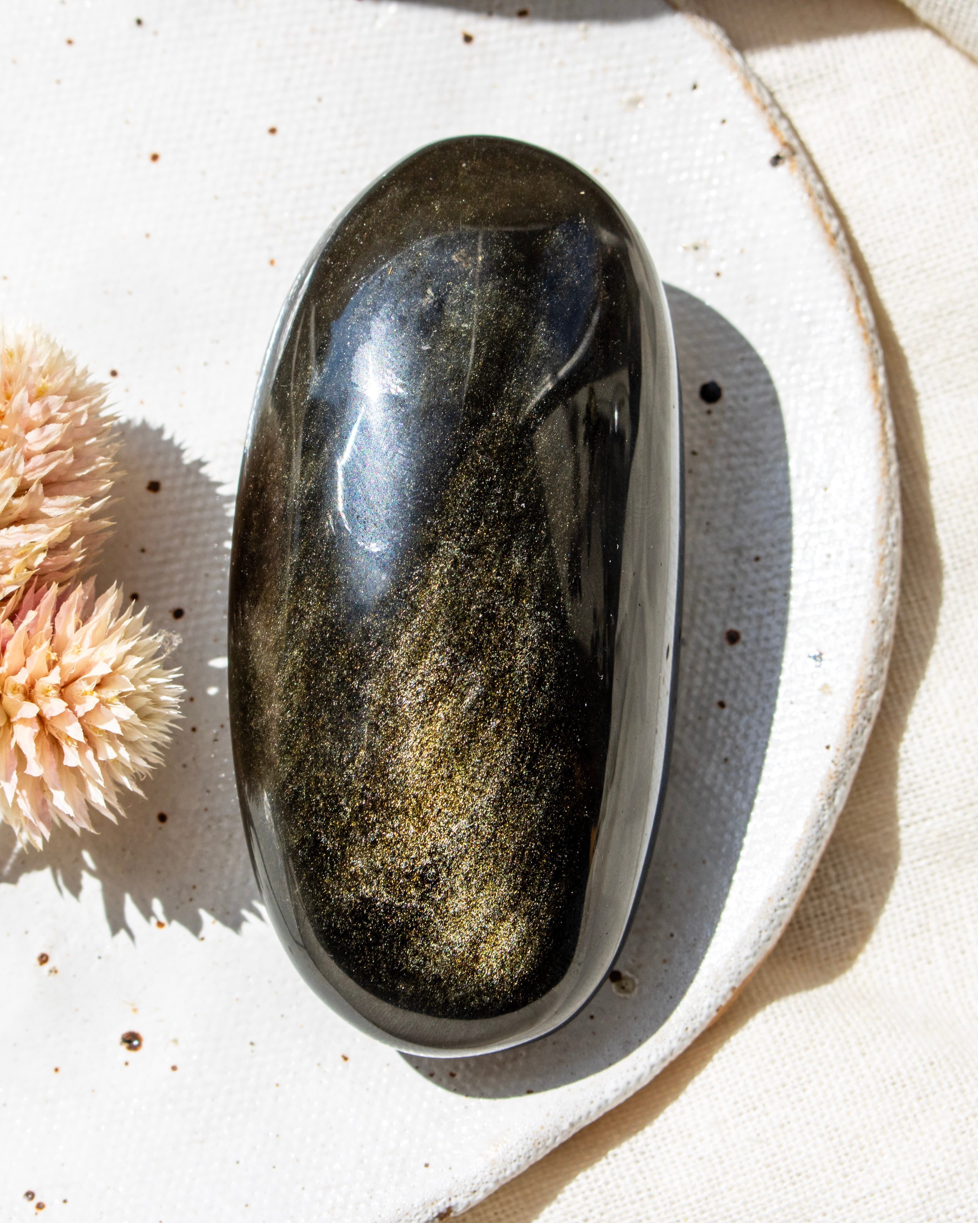 Polished stone in a white dish with dried flowers on a textured surface