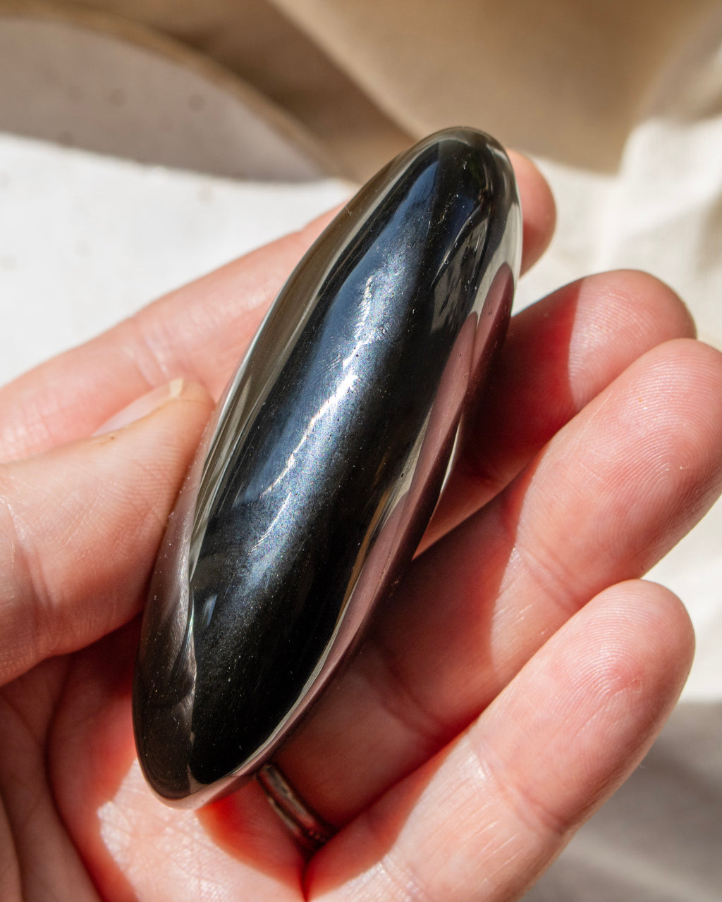 Hand holding a shiny, oval-shaped black stone against a neutral background