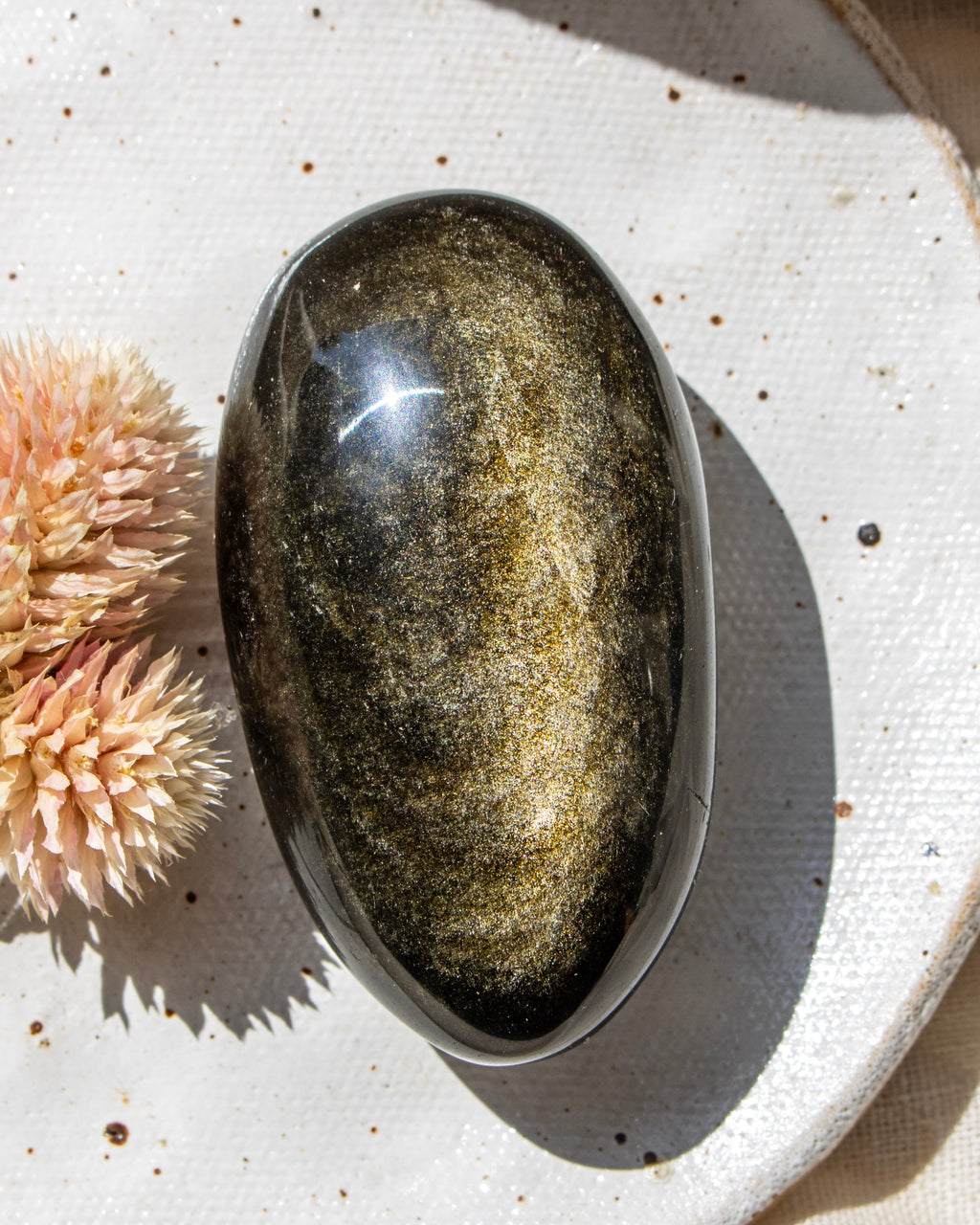 Oval-shaped stone on a textured surface with a dried flower