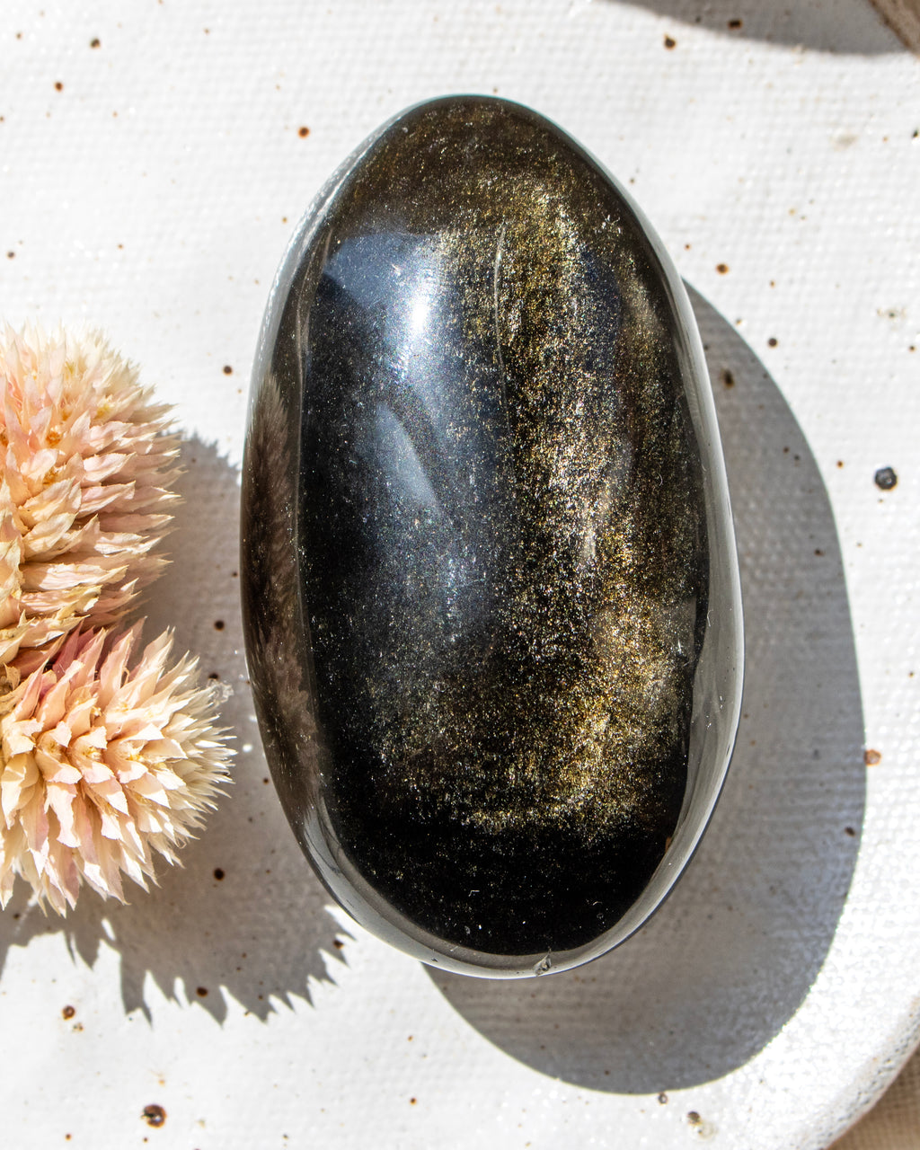Oval-shaped stone on a textured white surface with dried flowers.