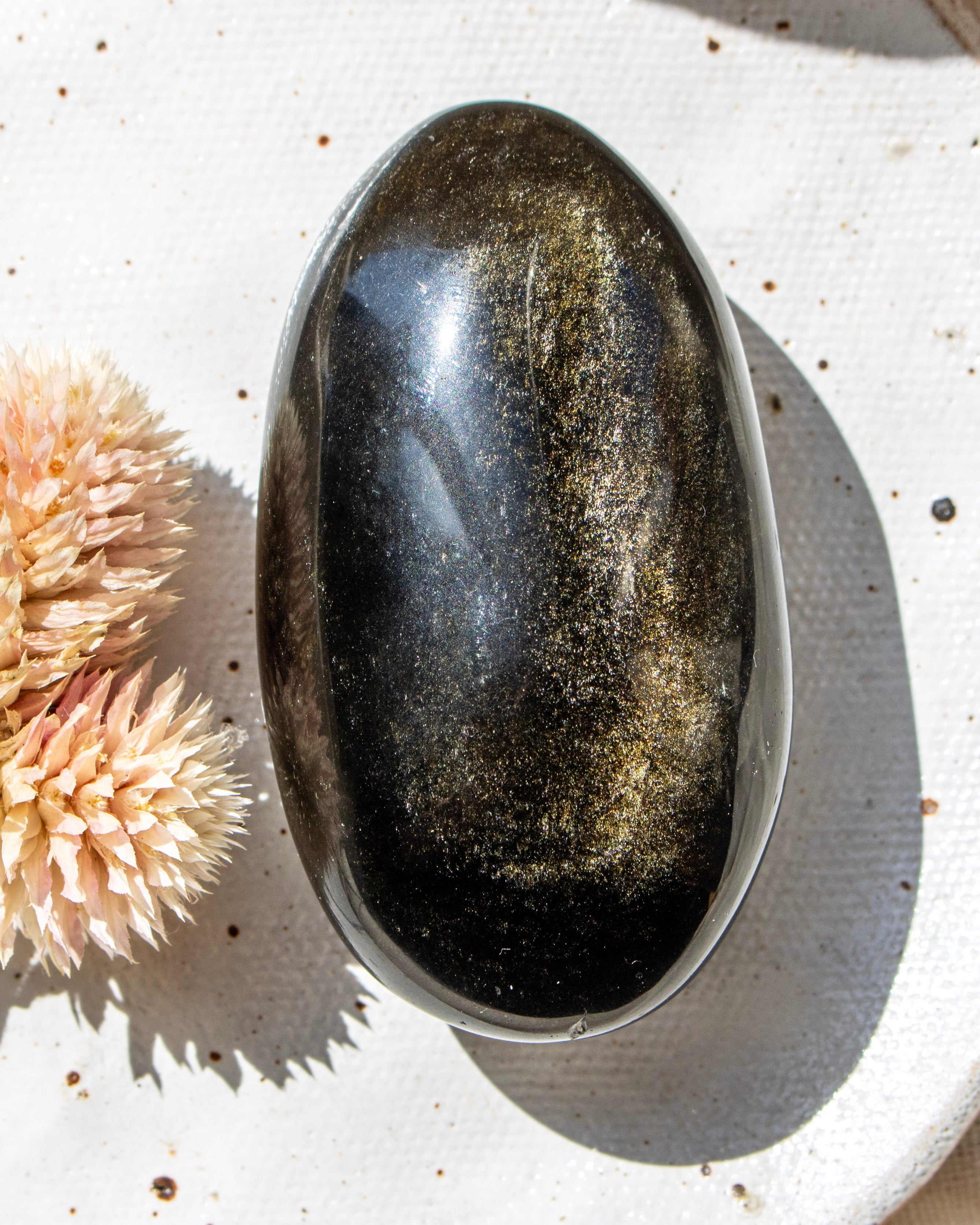 Oval-shaped stone on a textured white surface with dried flowers.
