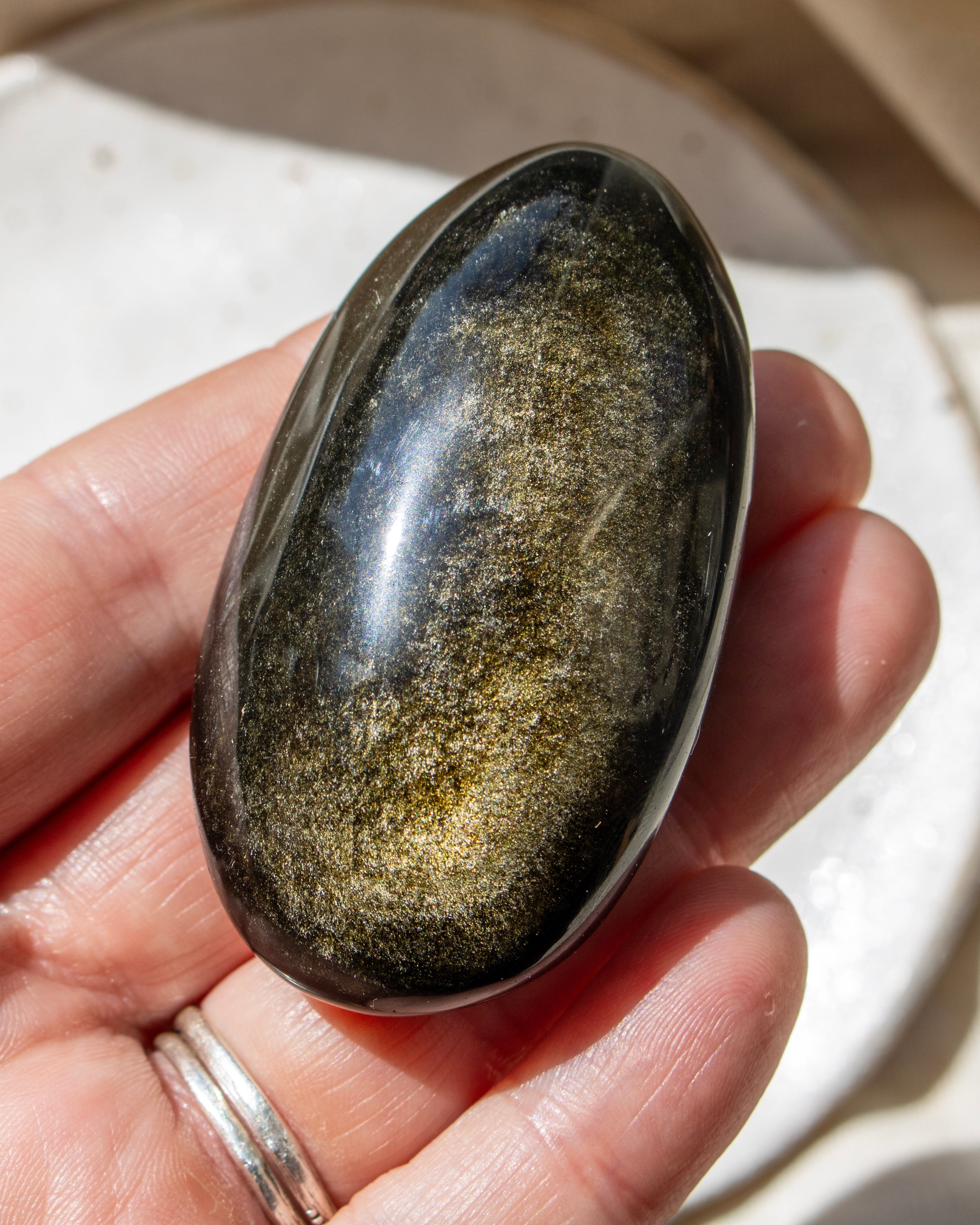 Person holding a polished stone with a silver setting against a neutral background
