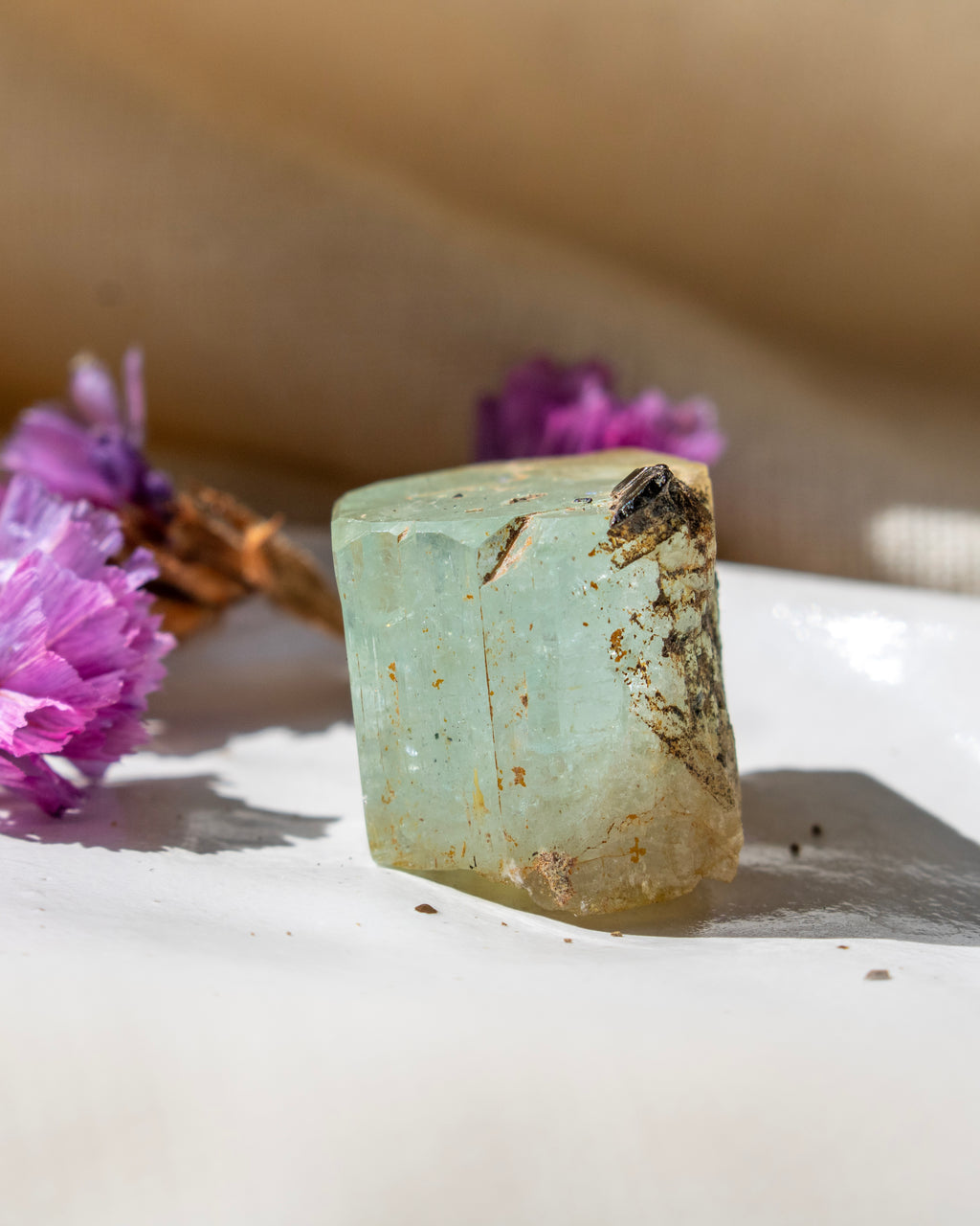 Green crystal on a white surface with purple flowers in the background