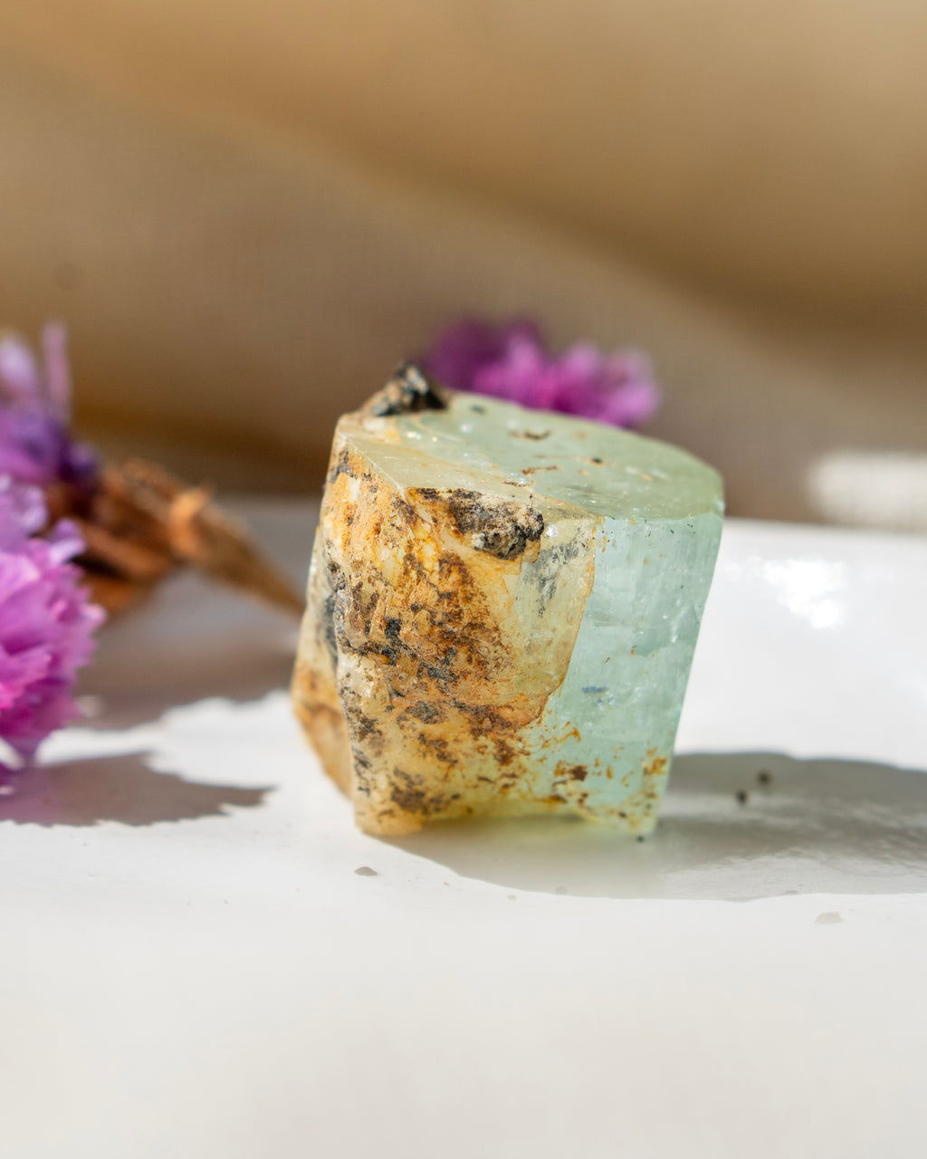 Mineral specimen on a white surface with purple flowers in the background