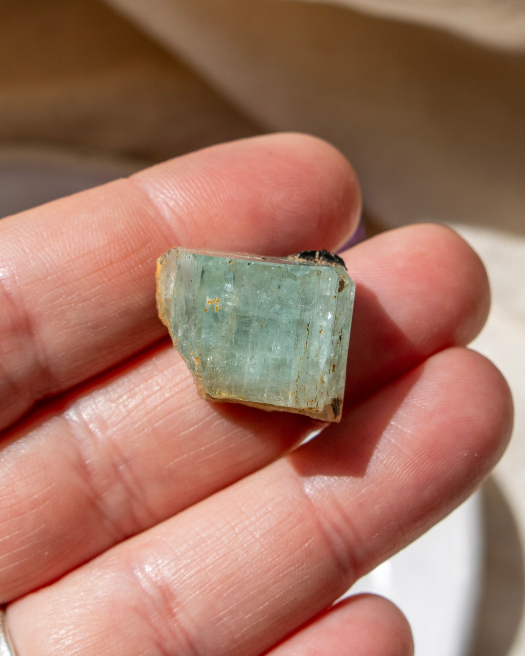 Small piece of greenish-blue crystal held between fingers against a neutral background