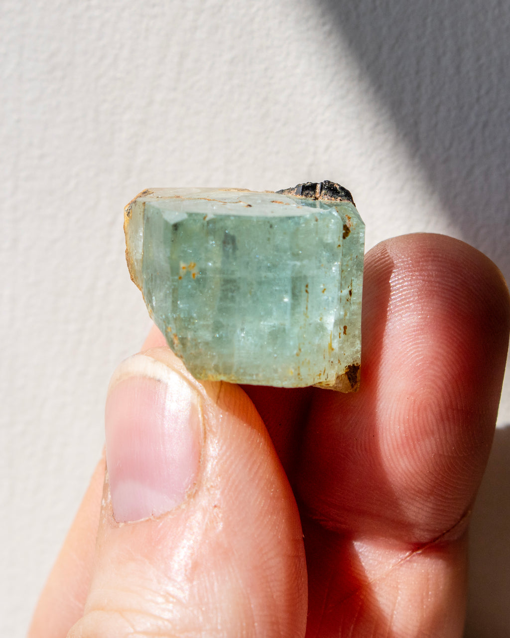 Hand holding a rough green gemstone against a neutral background