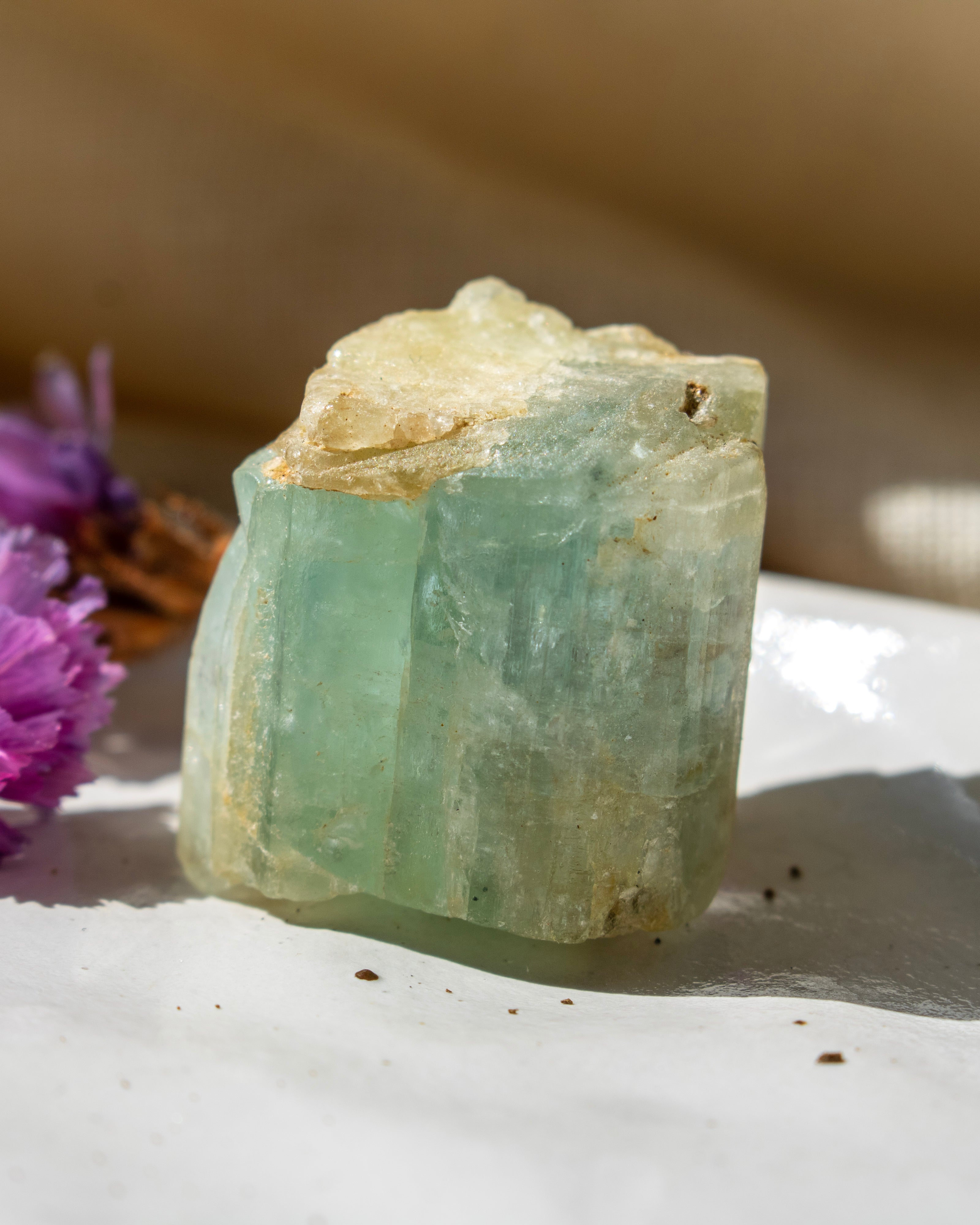 Raw green crystal on a white surface with a blurred background