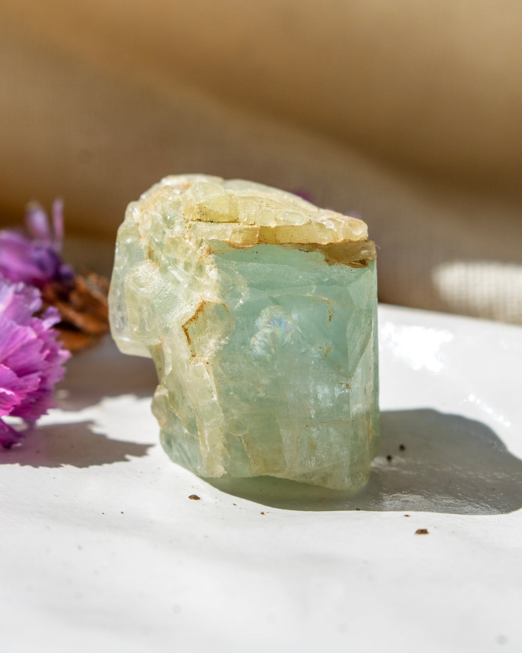 Raw crystal on a white surface with purple flowers in the background