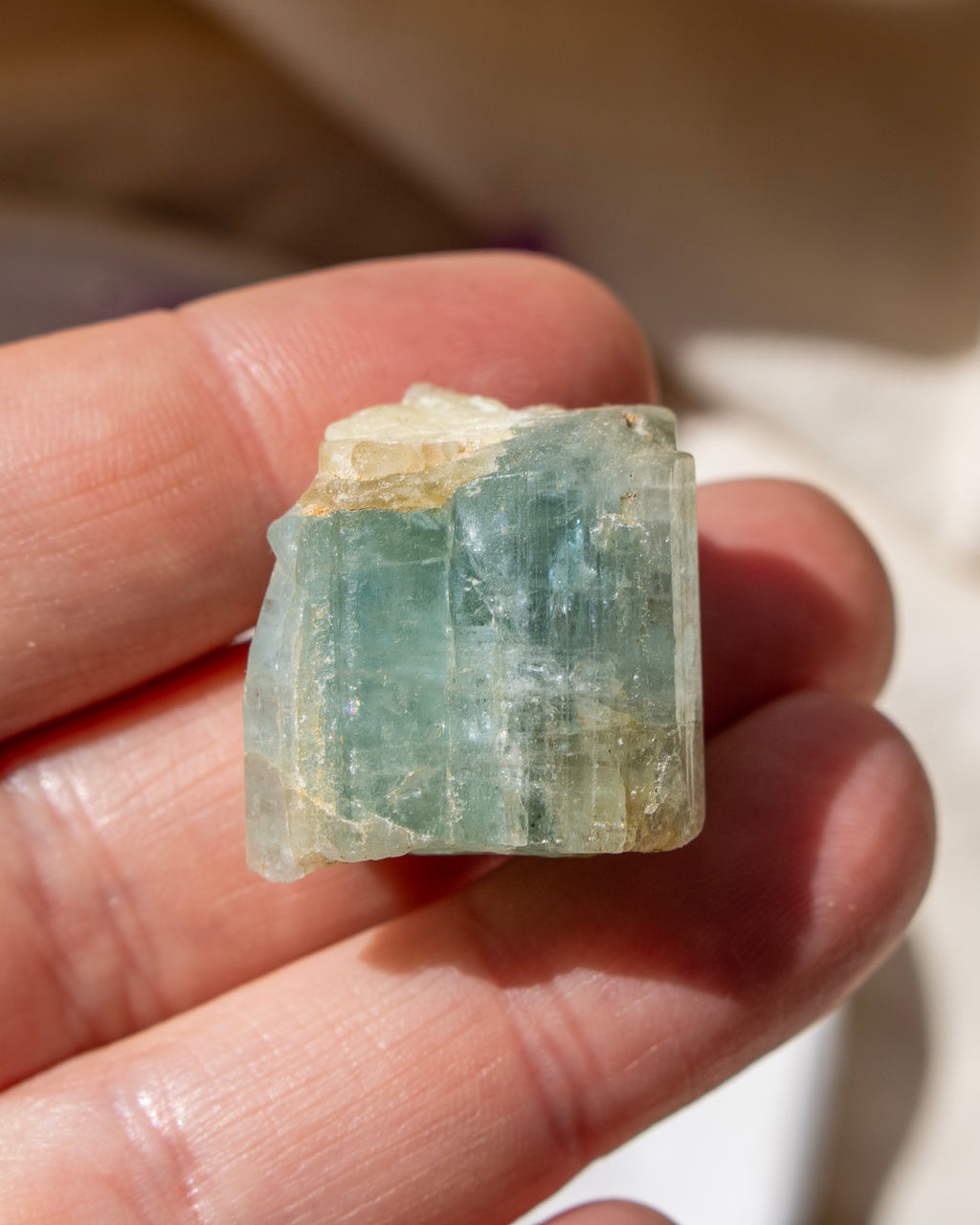 Raw crystal held between fingers with a blurred background