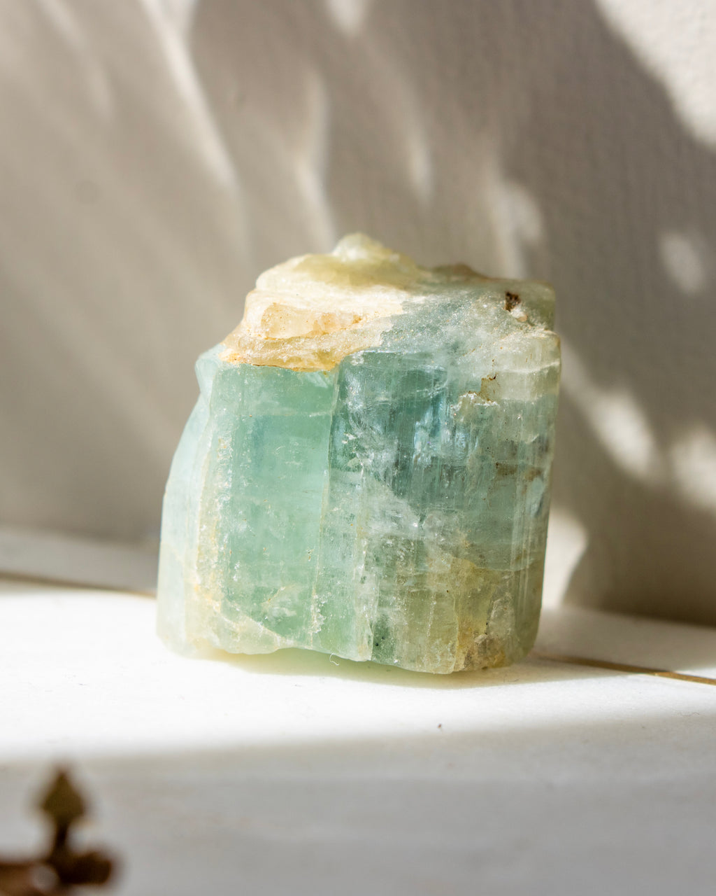 Raw green crystal on a white surface with soft shadows