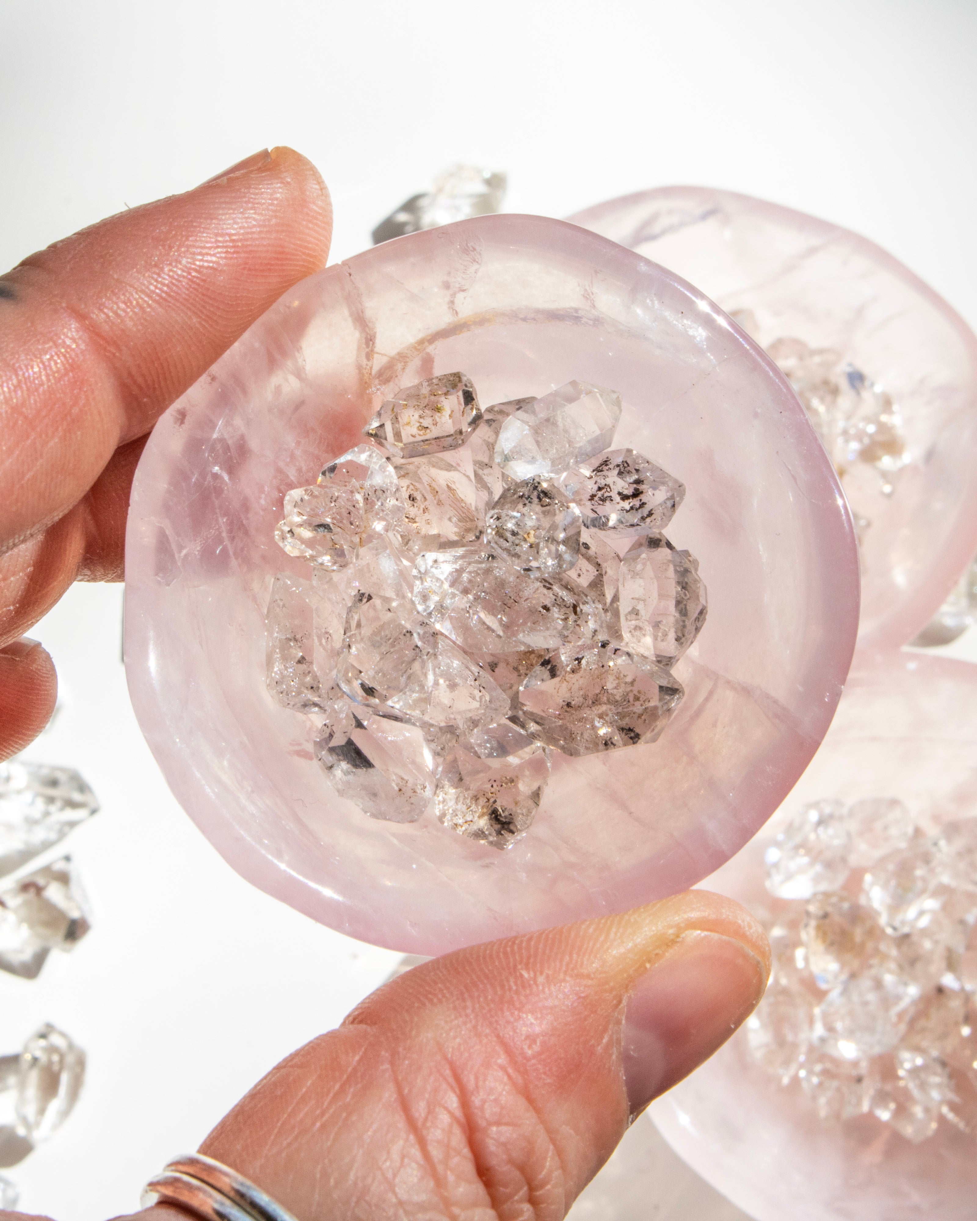Hand holding a pink crystal filled with clear crystals against a white background
