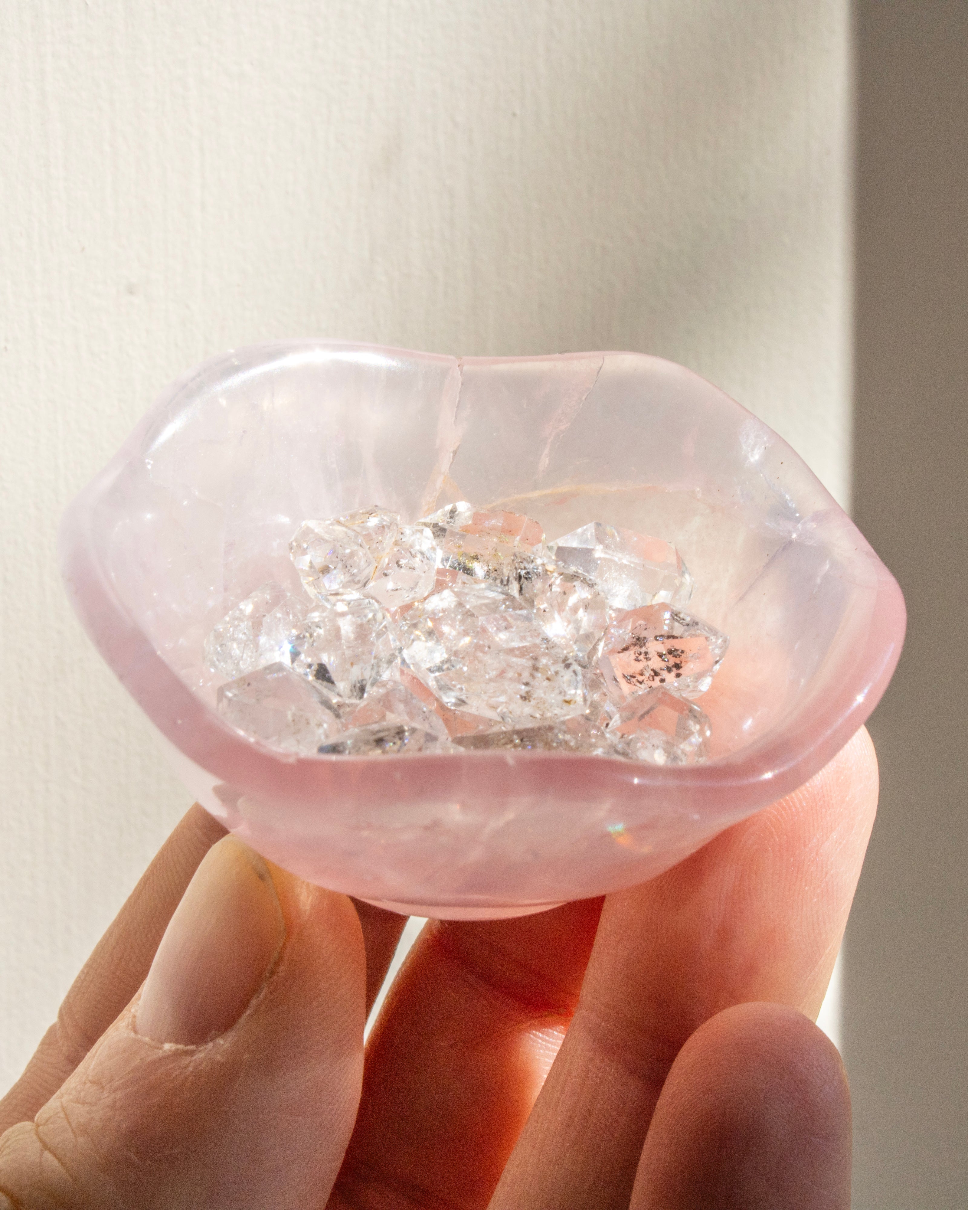 Hand holding a pink stone with embedded diamonds against a neutral background