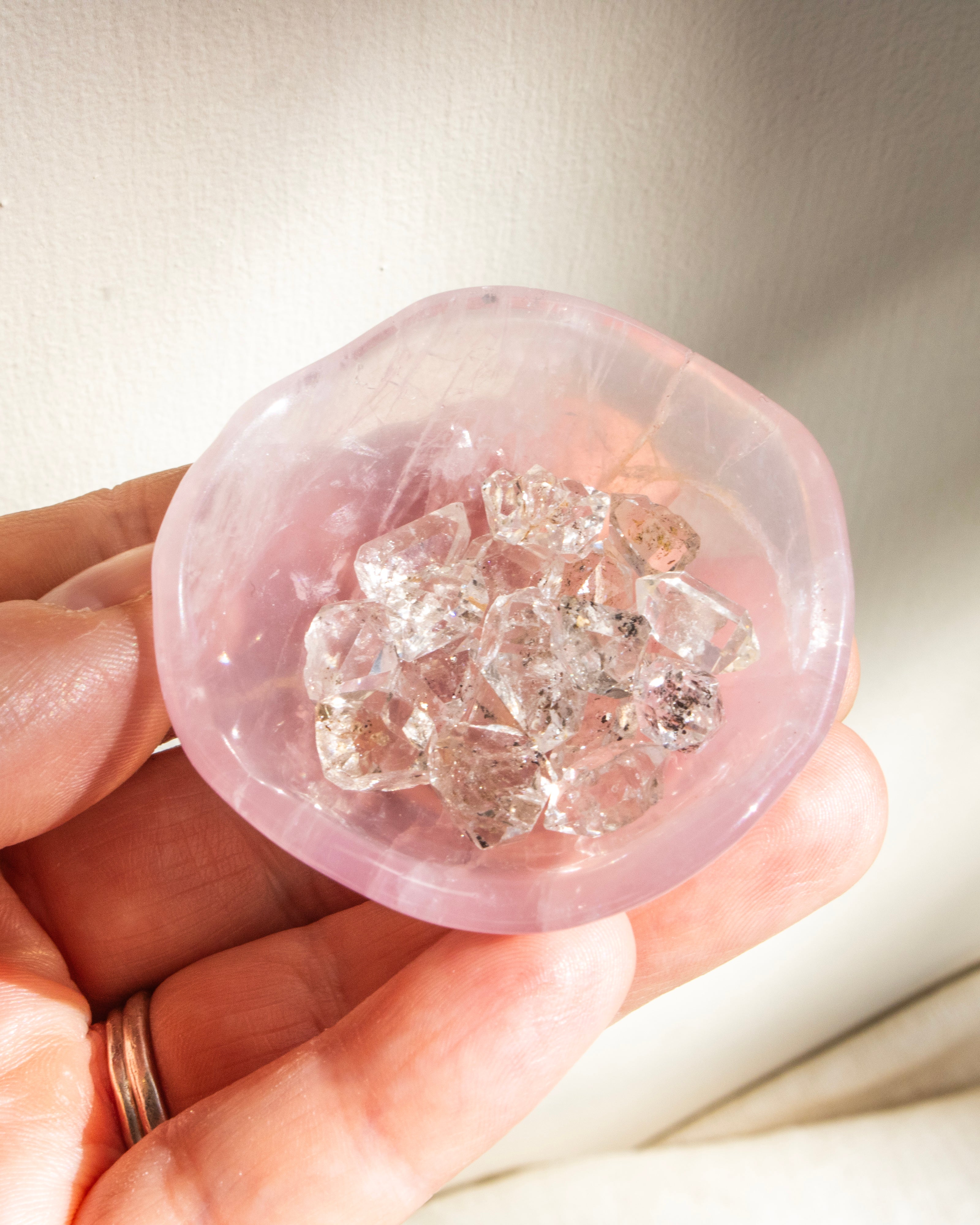 Hand holding a pink crystal with embedded clear crystals against a neutral background