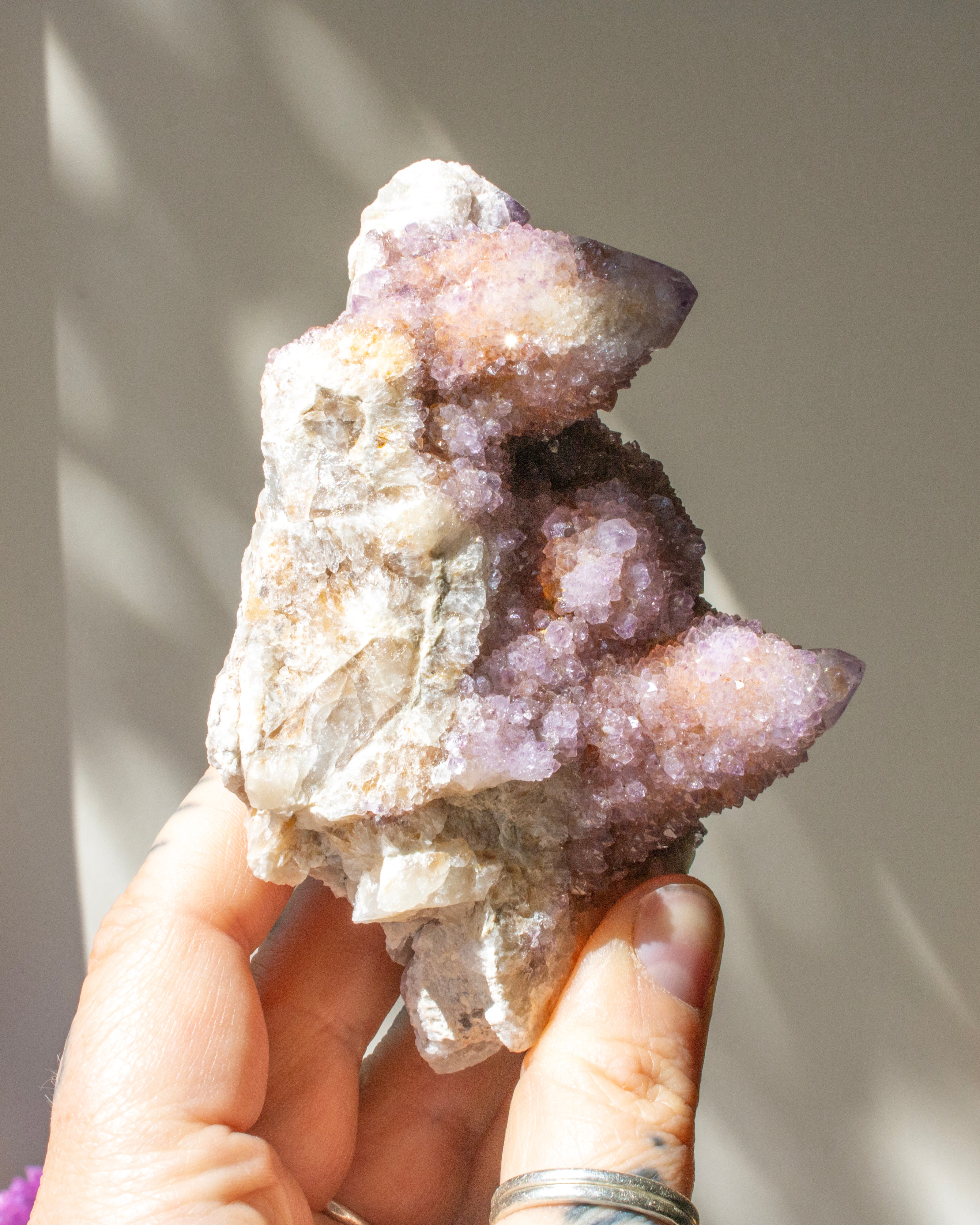 Hand holding a large crystal formation against a neutral background