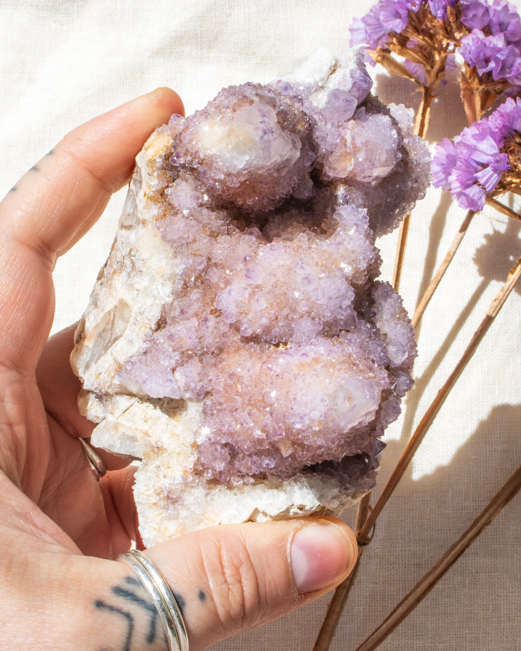 Hand holding a large crystal cluster with purple flowers in the background