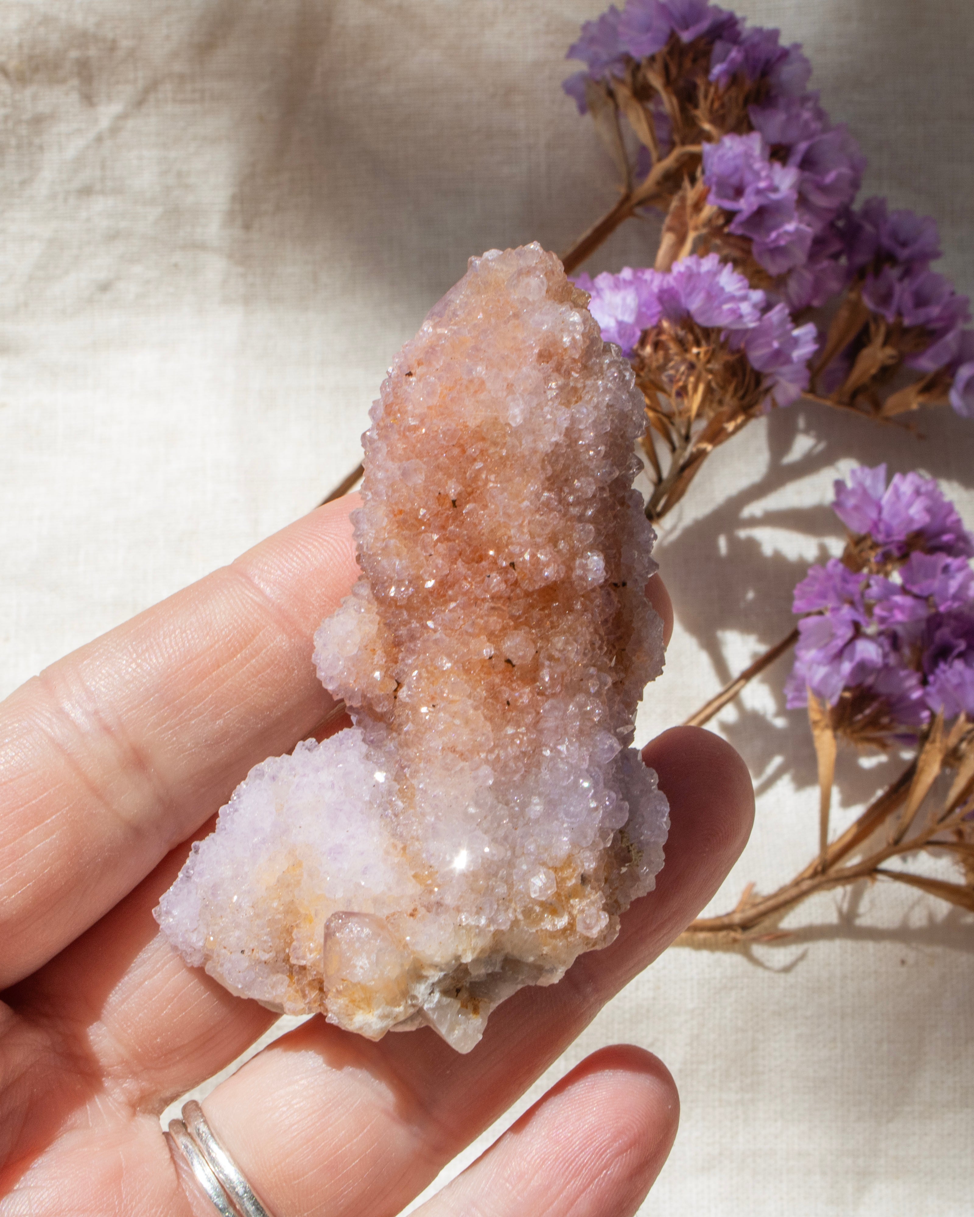 Hand holding a crystal with a beige and white coloration against a neutral background