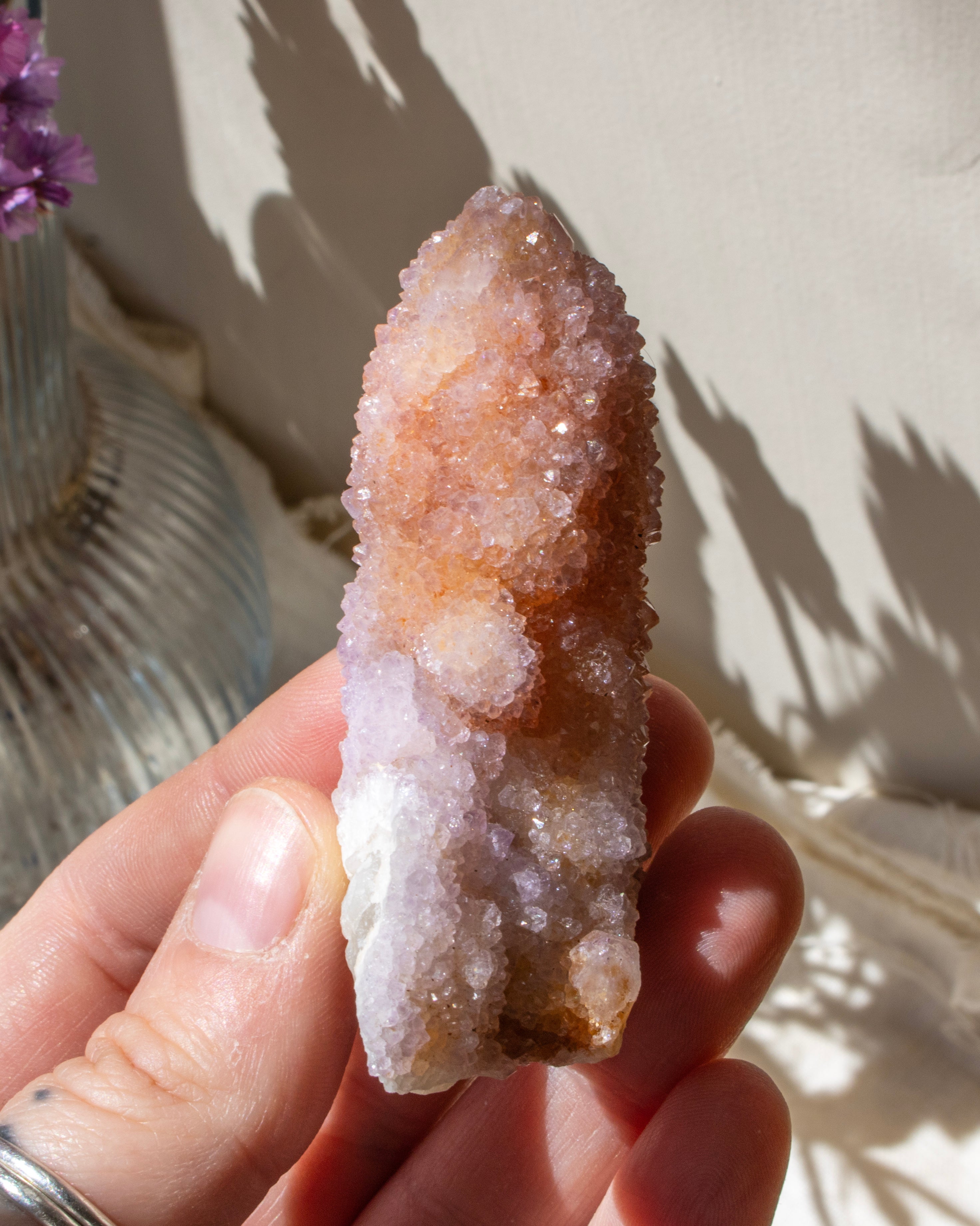 Hand holding a crystal with a beige and white coloration against a neutral background