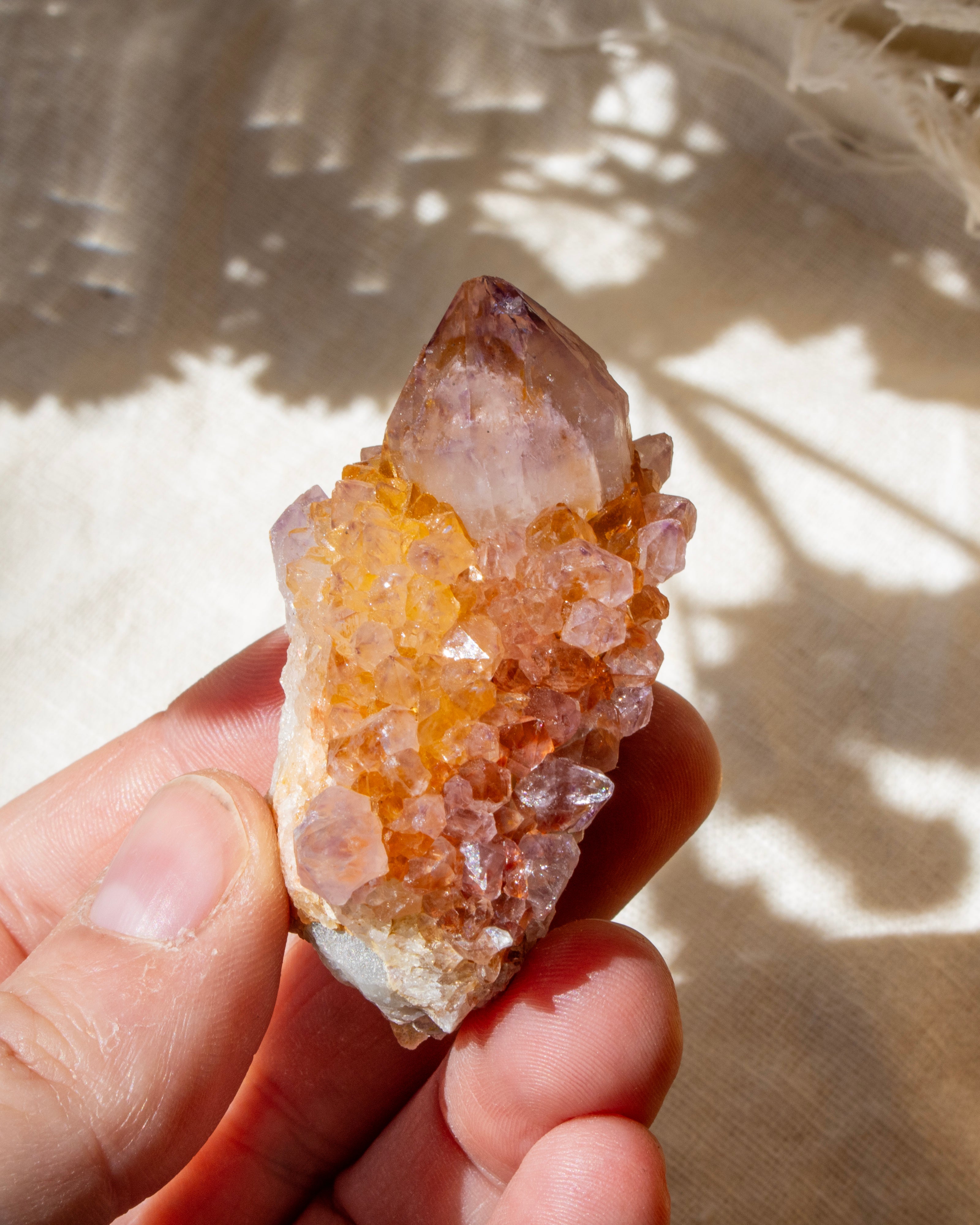 Hand holding a crystal with sunlight casting shadows on a textured surface