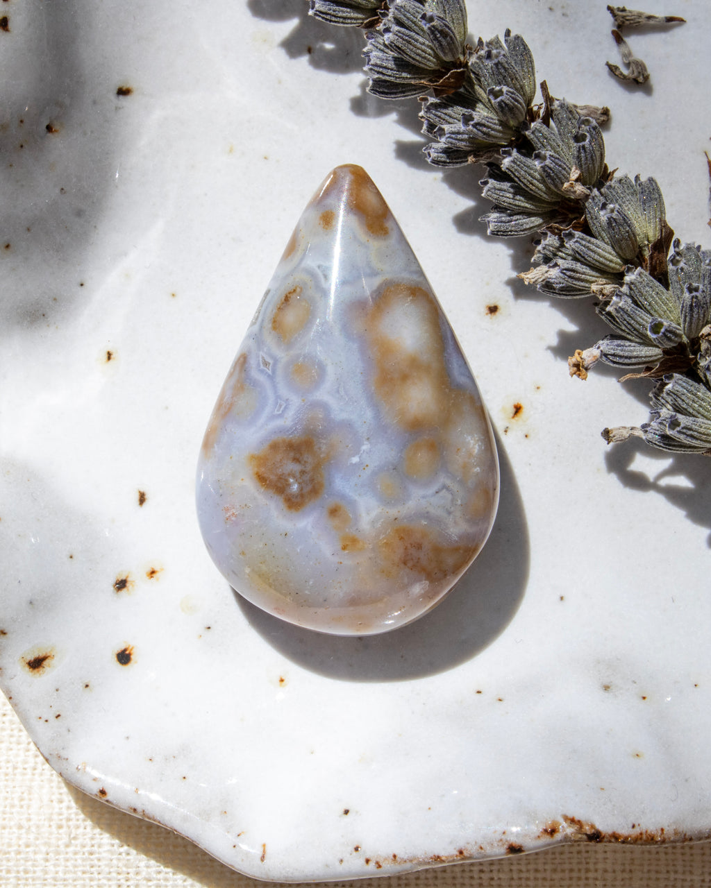 Teardrop-shaped agate stone on a textured surface with dried lavender.